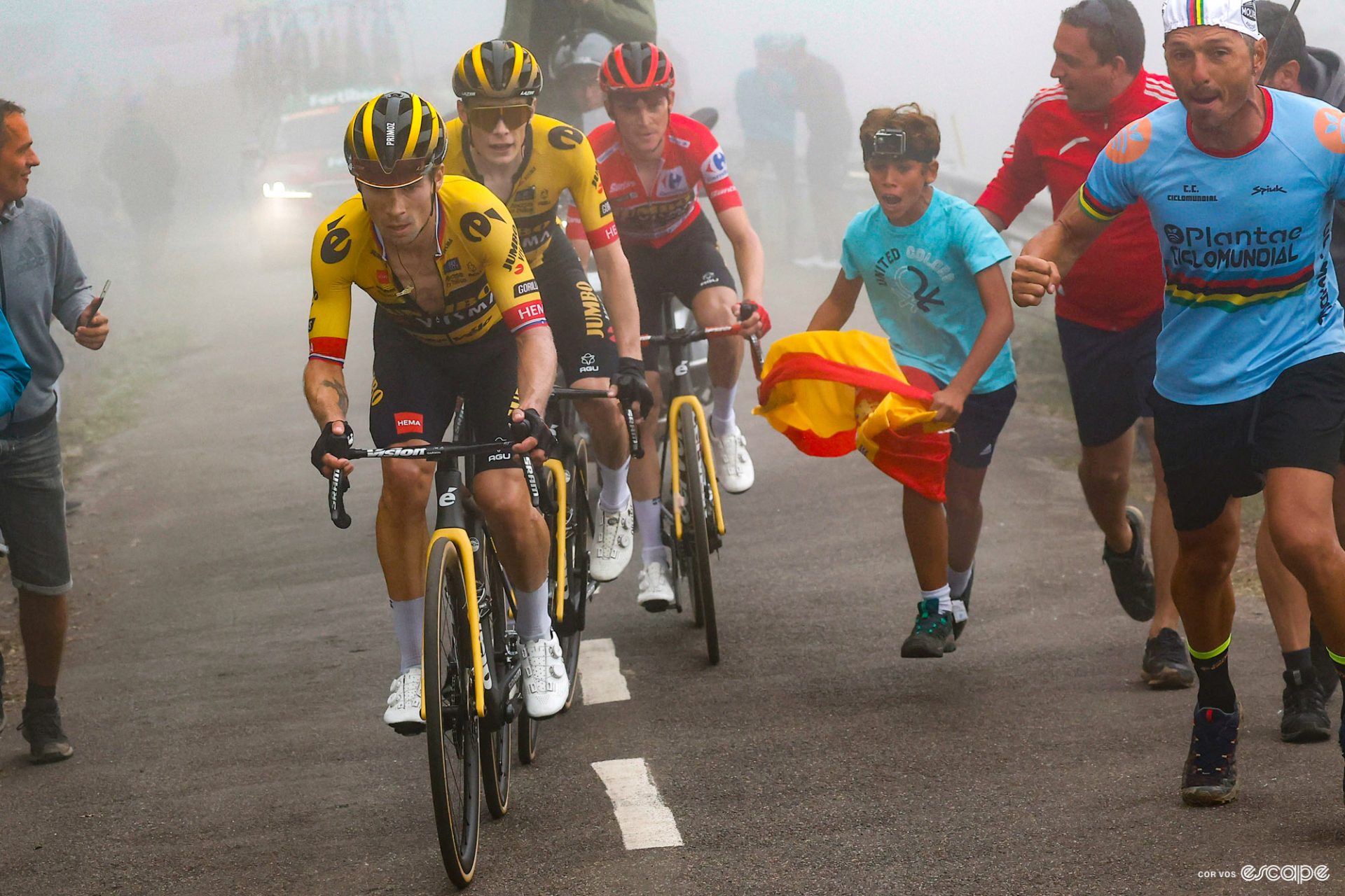 Primoz Roglic leads Jonas Vingegaard and Sepp Kuss, who is wearing the leader's red jersey, up the Angliru climb in foggy conditions.
