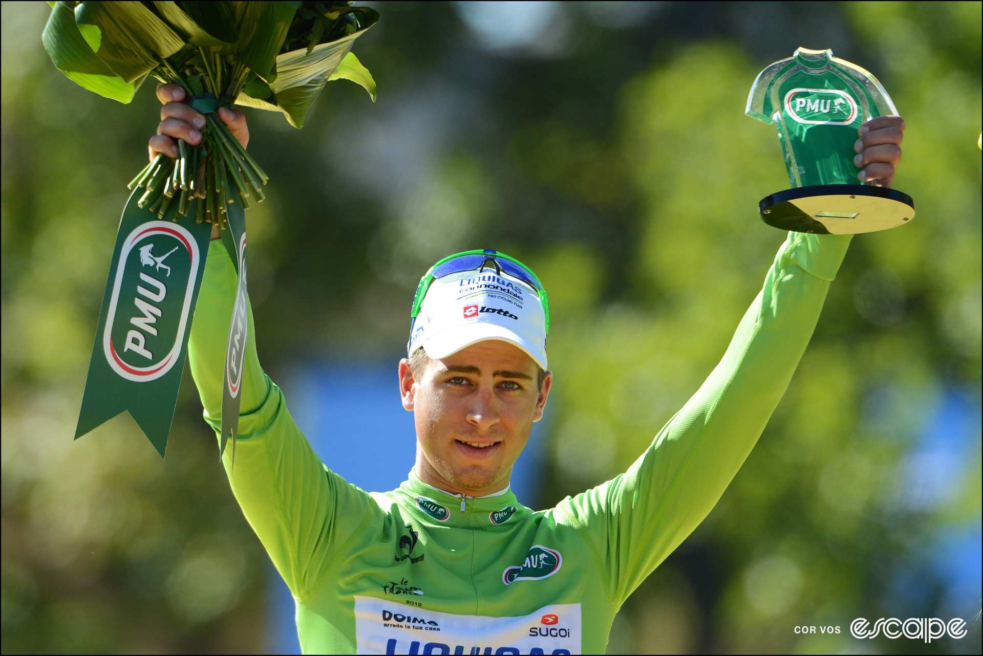 Peter Sagan on the final podium at the Tour de France in 2012, holding a bouquet of flowers, a small trophy, and wearing the green jersey.