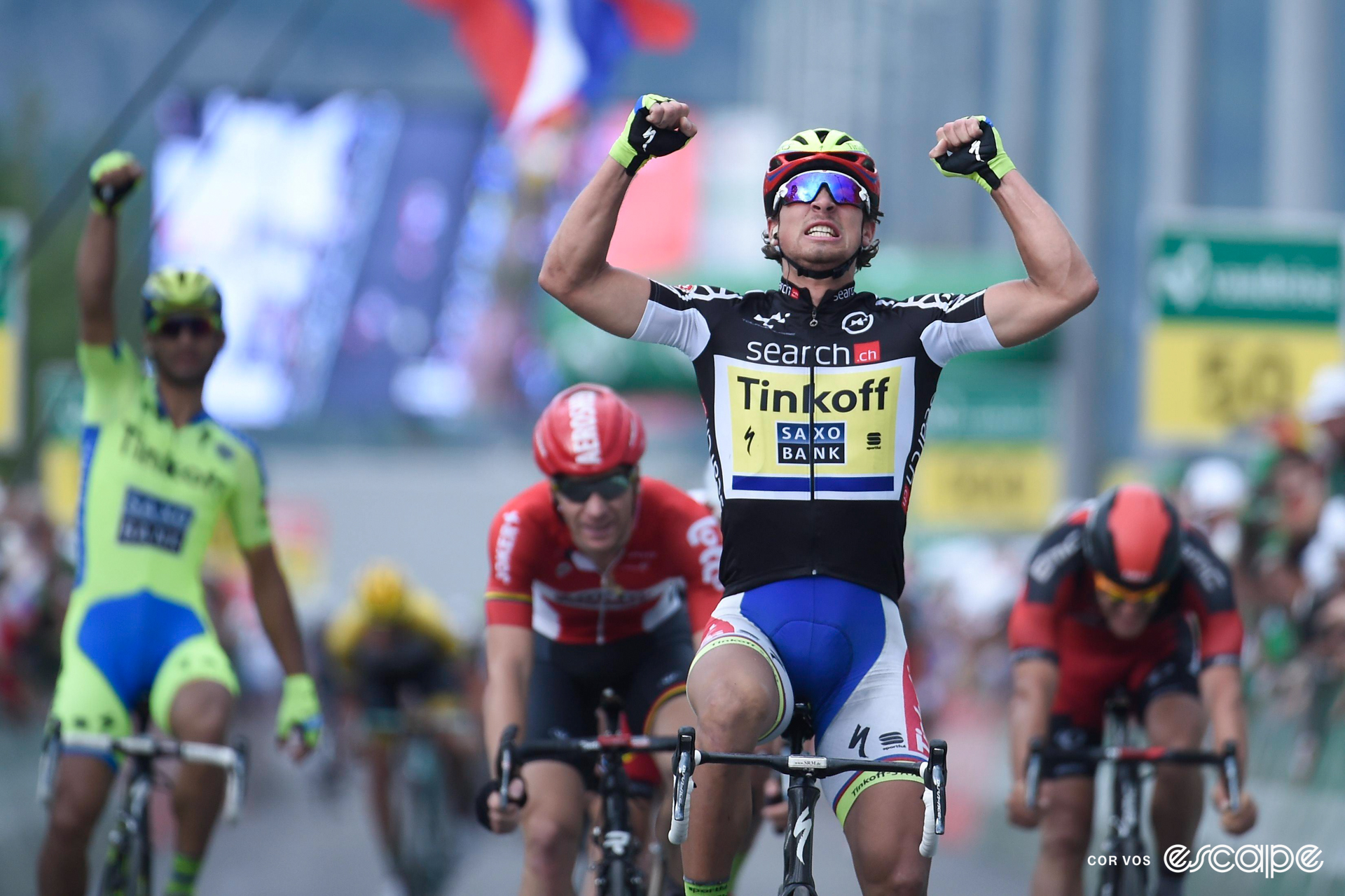 Peter Sagan celebrates winning a stage at the 2015 Tour de Suisse with a double overhead fist pump as a teammate celebrates out of focus in the background.