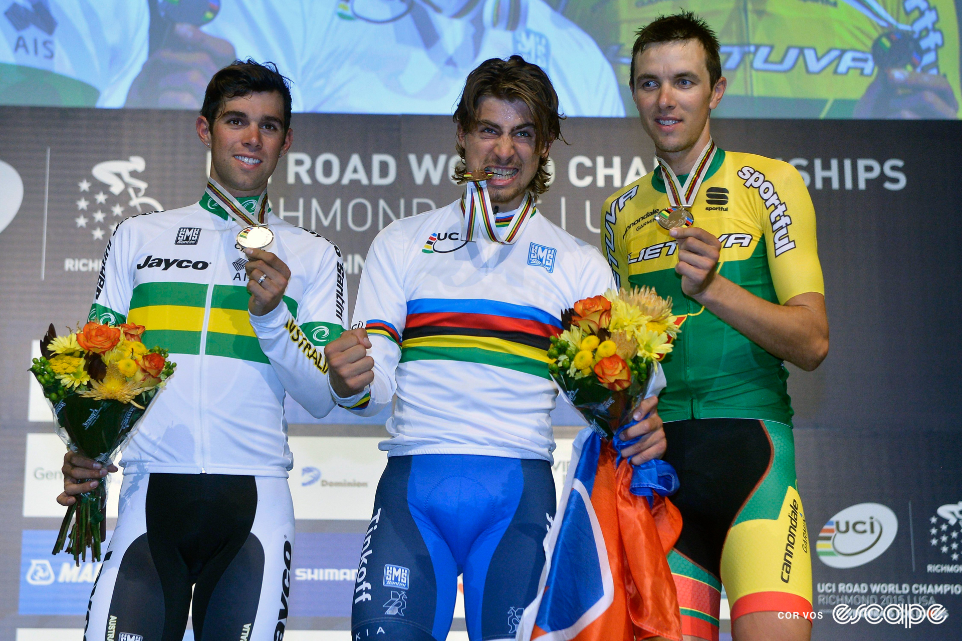 Peter Sagan bites on his gold medal on the podium after winning the 2015 world title. He's flanked by silver medalist Michael Matthews and bronze medalist Ramūnas Navardauskas.