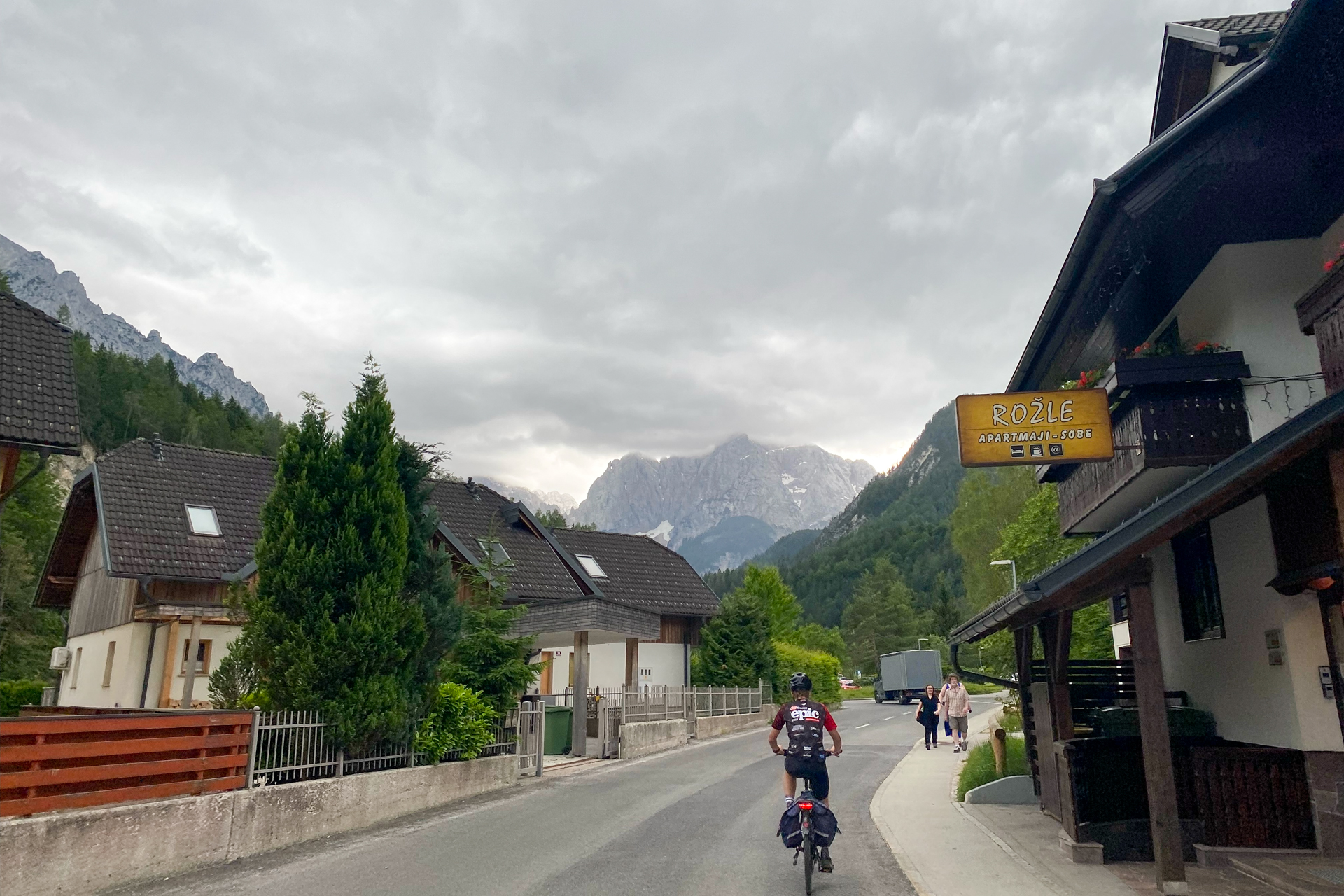 A lone cyclist rides through a small town with cloud-covered mountains in the background.