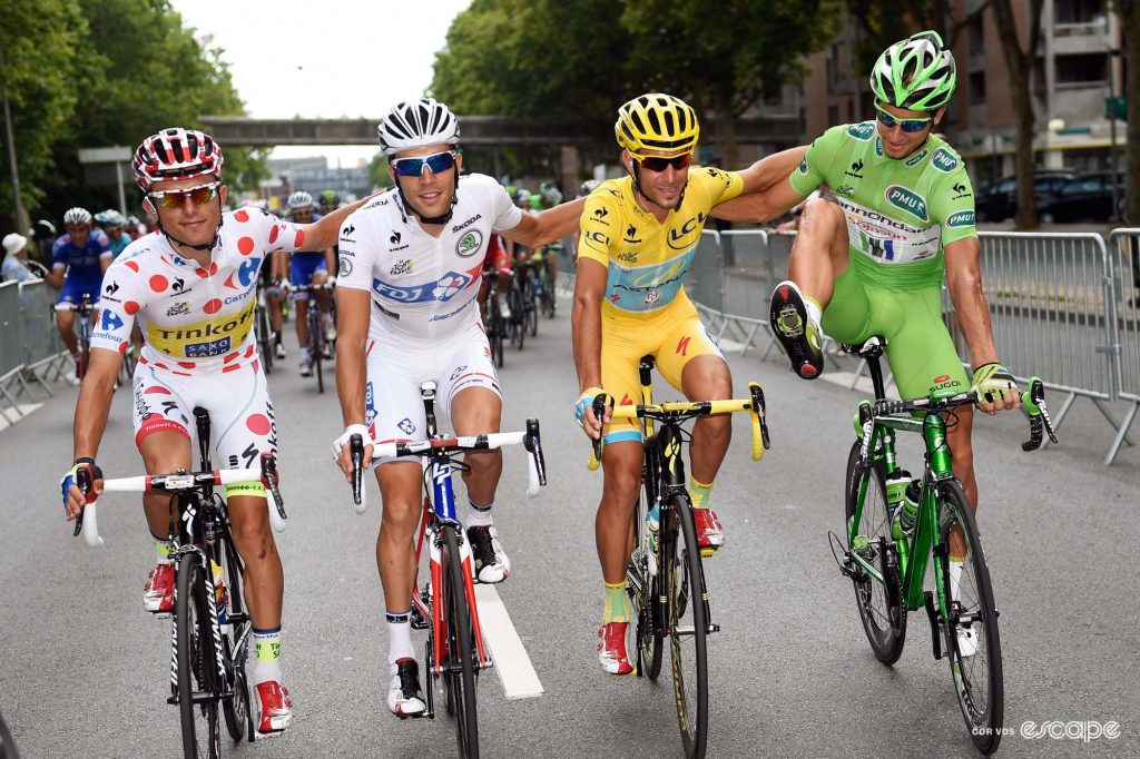 The winners of the four classifications at the Tour de France ride alongside each other in a posed photo, arms on each other's shoulders. Peter Sagan has one foot out of his pedal, waving it around for reasons unknown. 