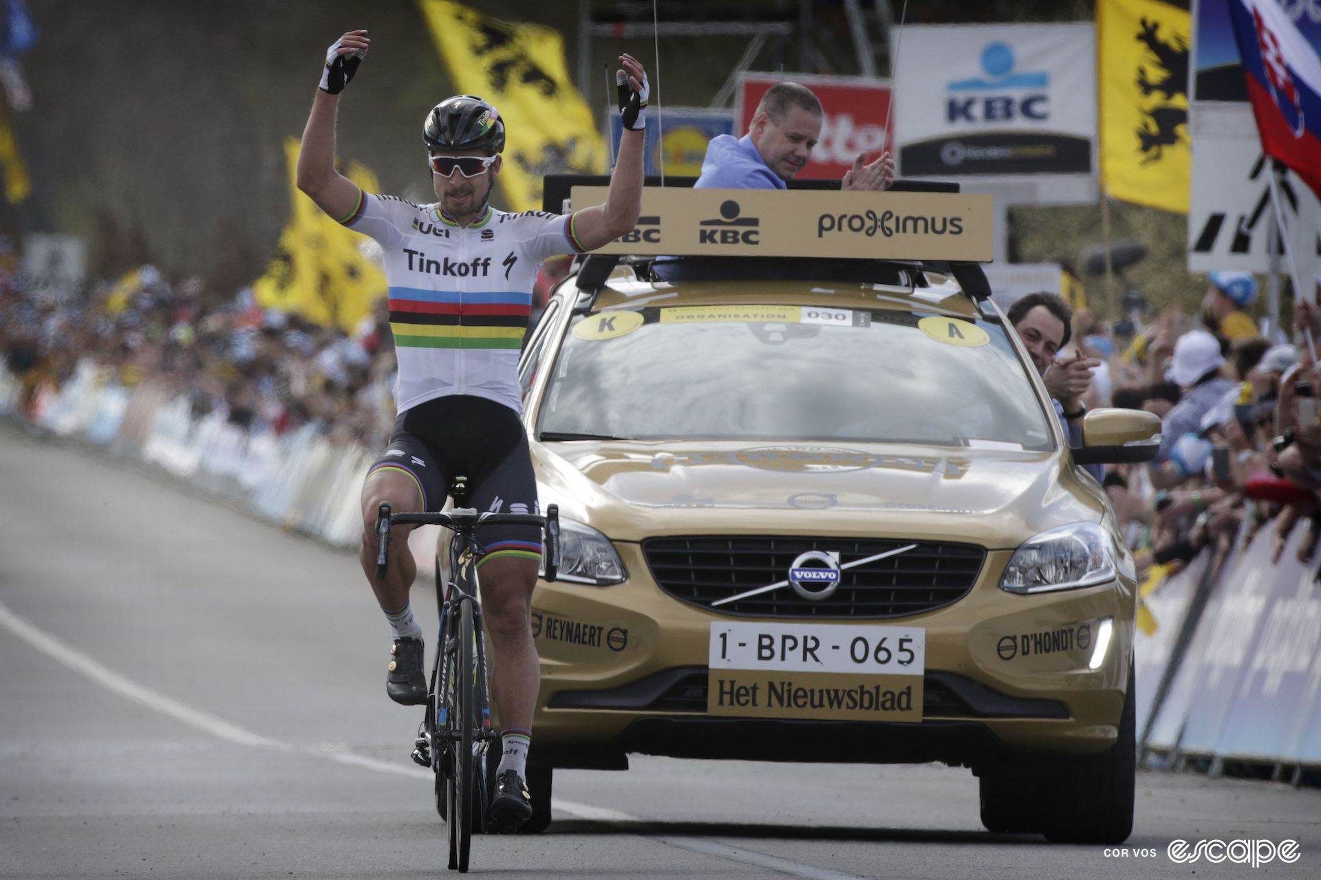 Peter Sagan celebrates winning the 2016 Tour of Flanders, solo, with two arms in the air, and the race director's car immediately behind him. The race director is clapping.