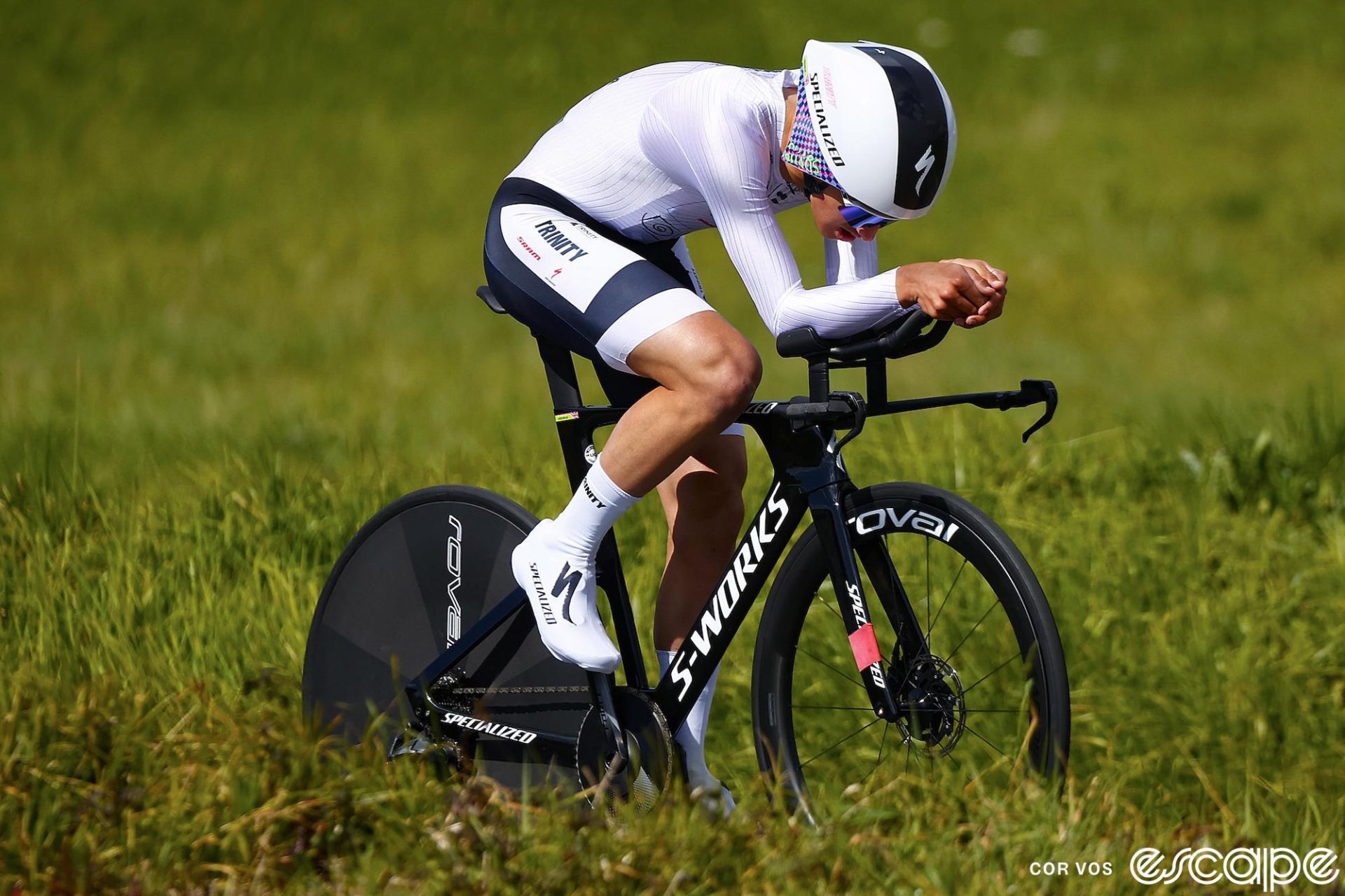 Lukas Nerurkar time trials at the O Gran Camiño stage race. He's in a white and black Trinity skinsuit on a Specialized Shiv, head down in an aero tuck.