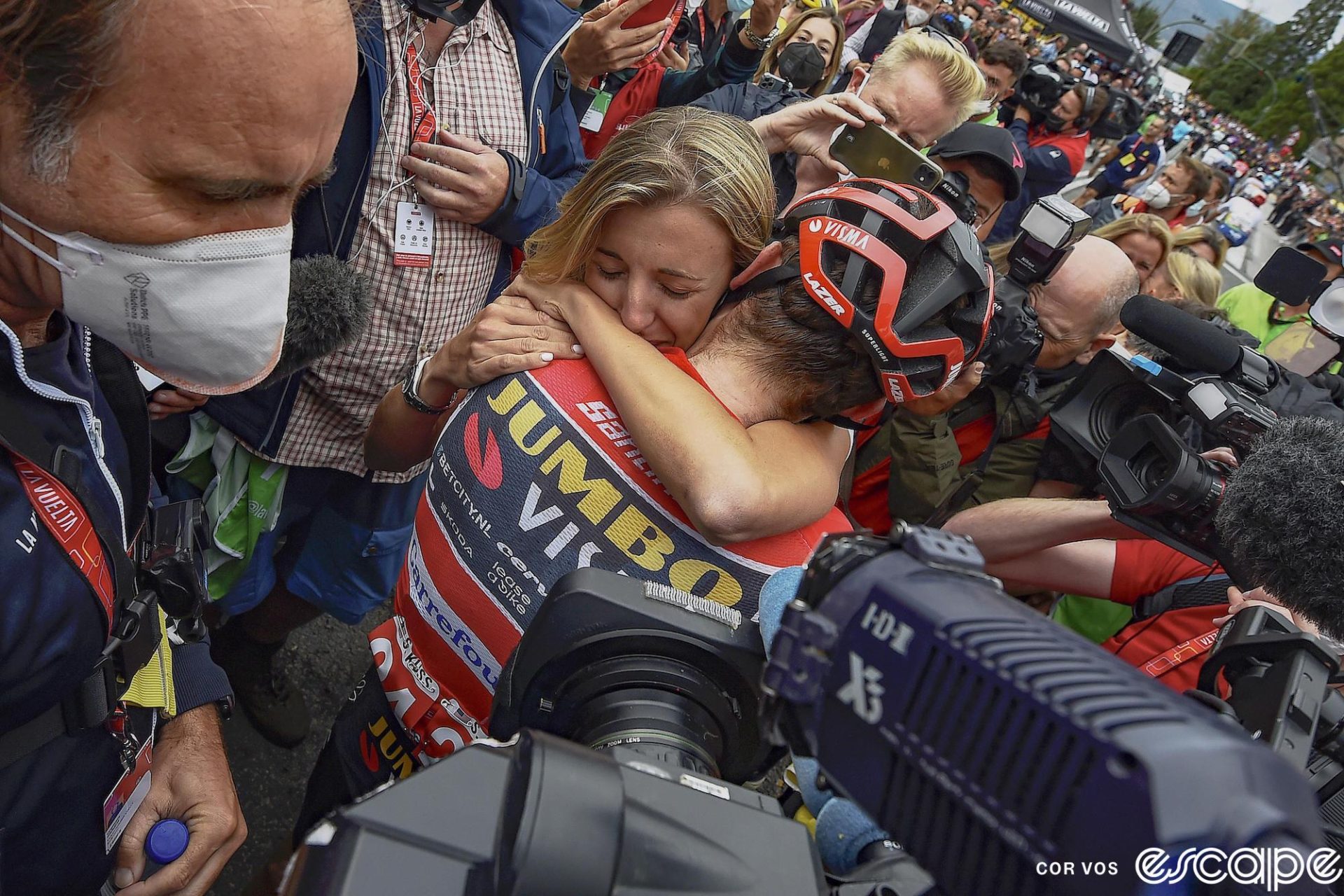 Sepp Kuss embraces his wife, Noemi, after a stage at the 2023 Vuelta a España. They're surrounded by a crowd of media.