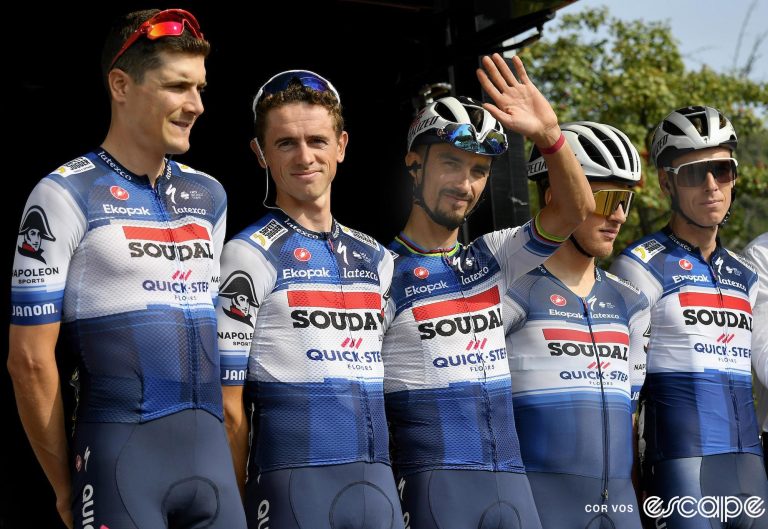 Julian Alaphilippe waves at sign-in for the Tre Valle Varesine race in Italy, alongside four of his Soudal Quick-Step teammates. He has a somewhat wistful expression.