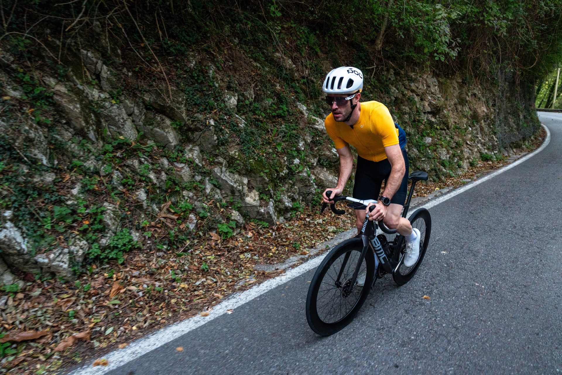 The photo shows the writer climbing out of the saddle on the new BMC TeamMachine R 01 on a quiet Italian road with an overgrown rock face along side the road.