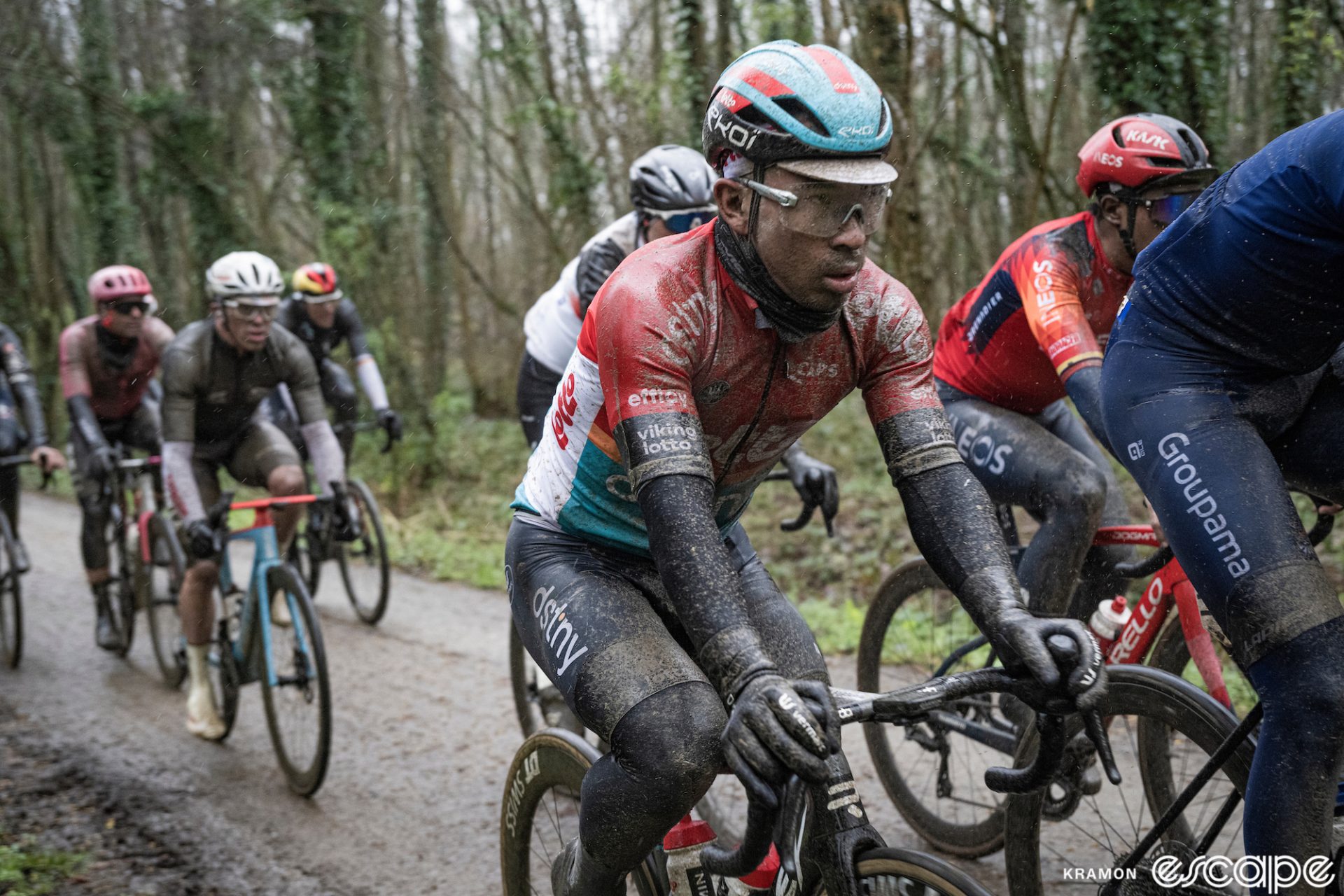Caleb Ewan rides muddy cobbles in the 2023 Gent-Wevelgem. He looks absolutely miserable, sopping wet and covered in grime, and has a faraway look on his face.