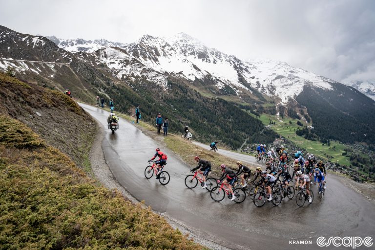 The pack rides up a wet road to a snowy summit in the 2023 Giro d'Italia.