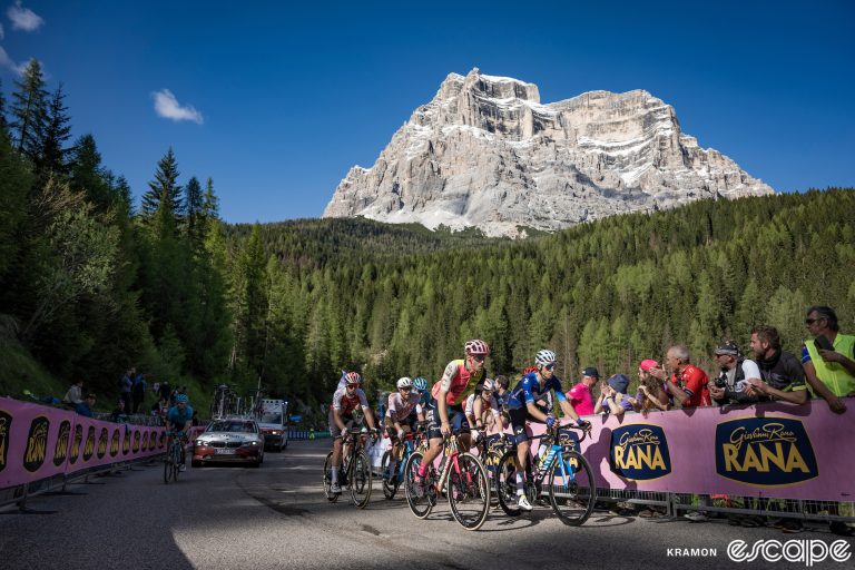 Riders climb in the 2023 Giro d'Italia. They're passing a distinctive pink sponsor banner, and behind them looms a distinctively Dolomite-looking mountain.