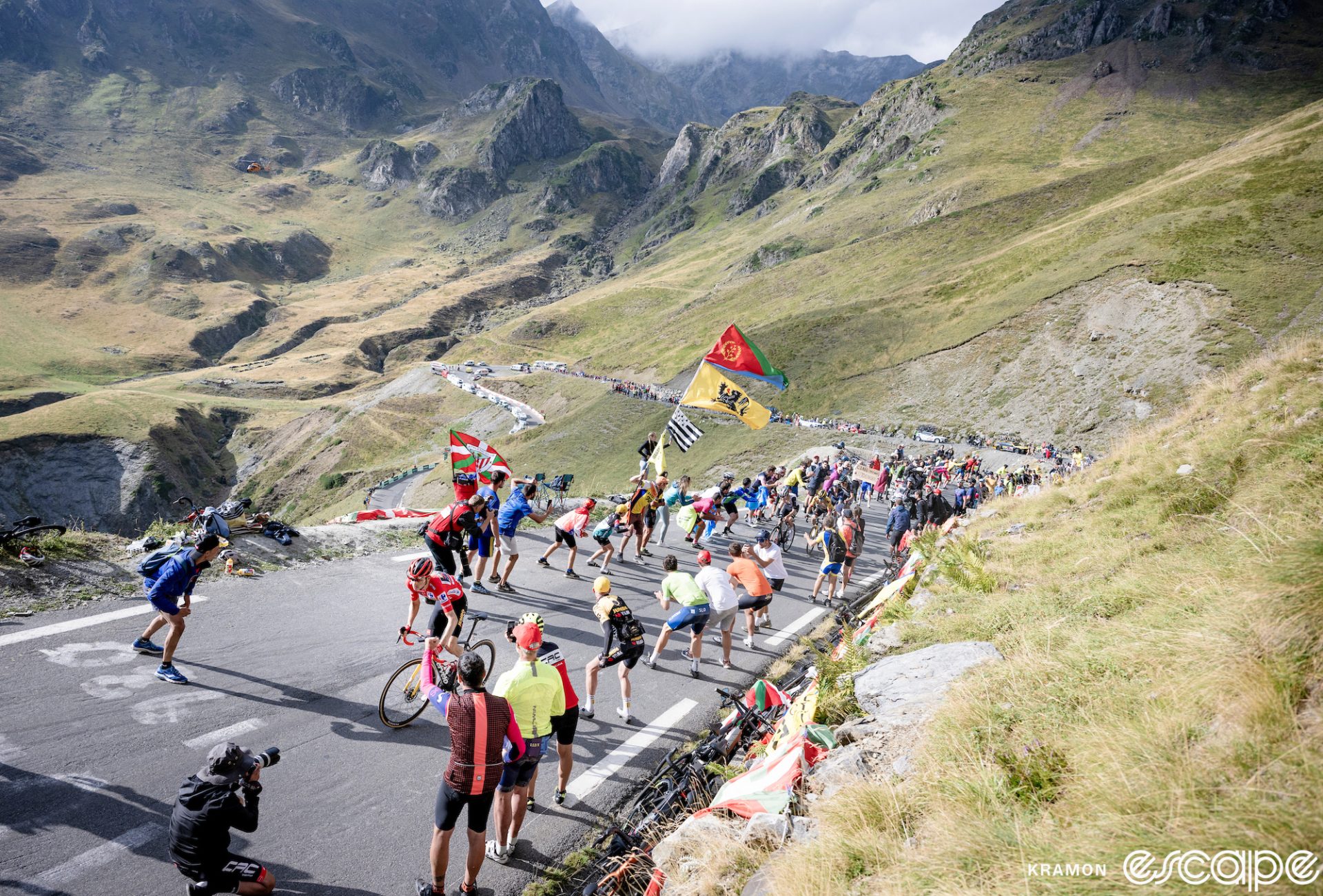 Sepp Kuss climbs the Col du Tourmalet at the 2023 Vuelta a España. He's alone, riding away from his pursuers in front of a line of fans, with rugged Pyreneean peaks and the road switchbacking down the mountain in the background.