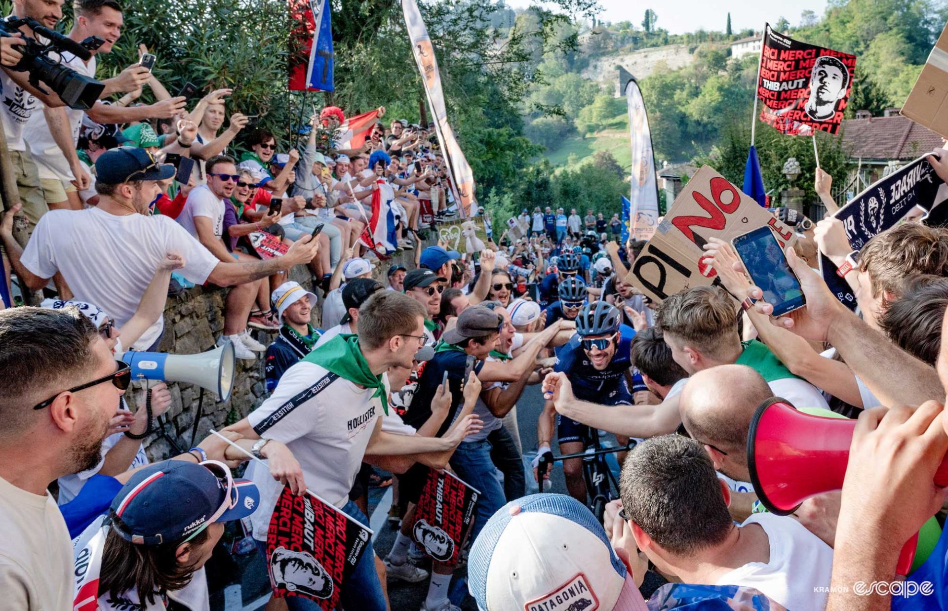 Thibaut Pinot at the centre of a swarm of flags, waving hands, and signs crowding the road.
