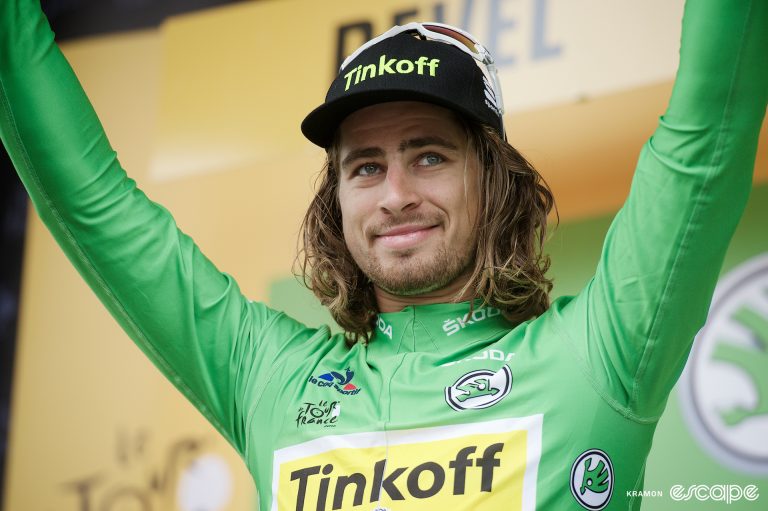 Peter Sagan wearing the green jersey on stage at the Tour de France, with his arms aloft.