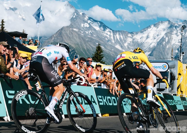 Jonas Vingegaard and Tadej Pogačar sprint for the finish on stage 16 of the 2023 Tour de France at Morzine. They're shown from the back, diving toward the line in front of a crowd of fans, with snowy Alpine peaks looming in the background.