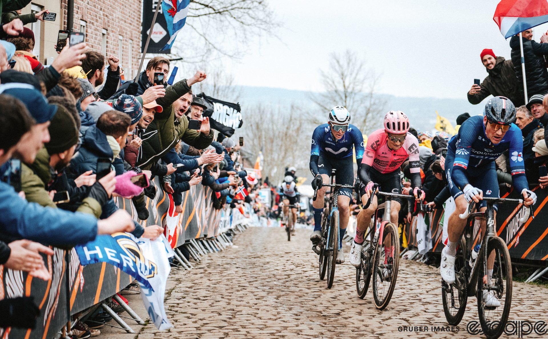 Matteo Jorgenson follows Neilson Powless and Stefan Küng up a cobbled climb at the 2023 Tour of Flanders, as fans line both sides of the lane and cheer.