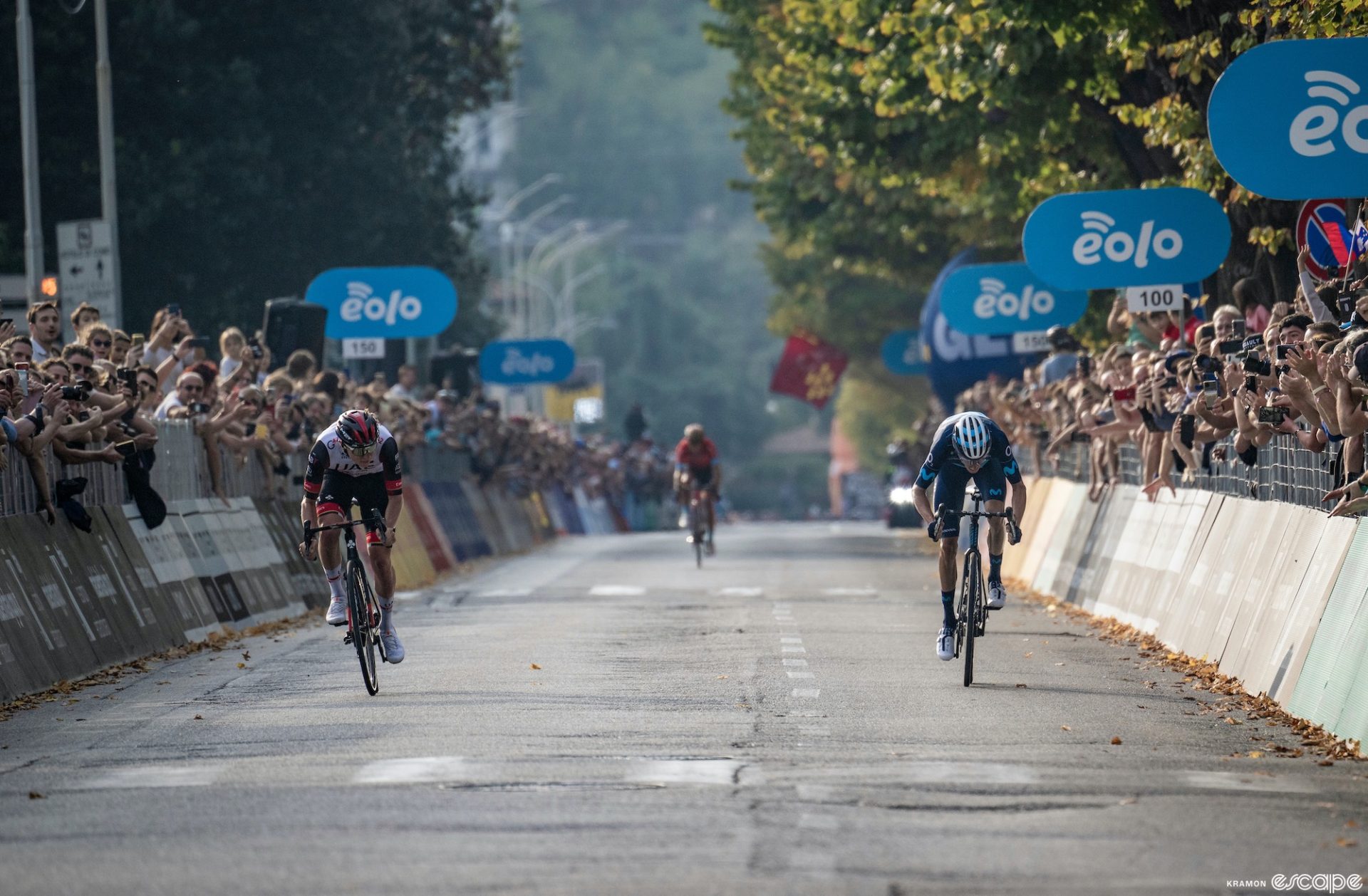 Tadej Pogačar sprinting against Enric Mas in the finale of the 2022 Il Lombardia. They're on opposite sides of the road and Pogačar is looking slightly across at his rival.