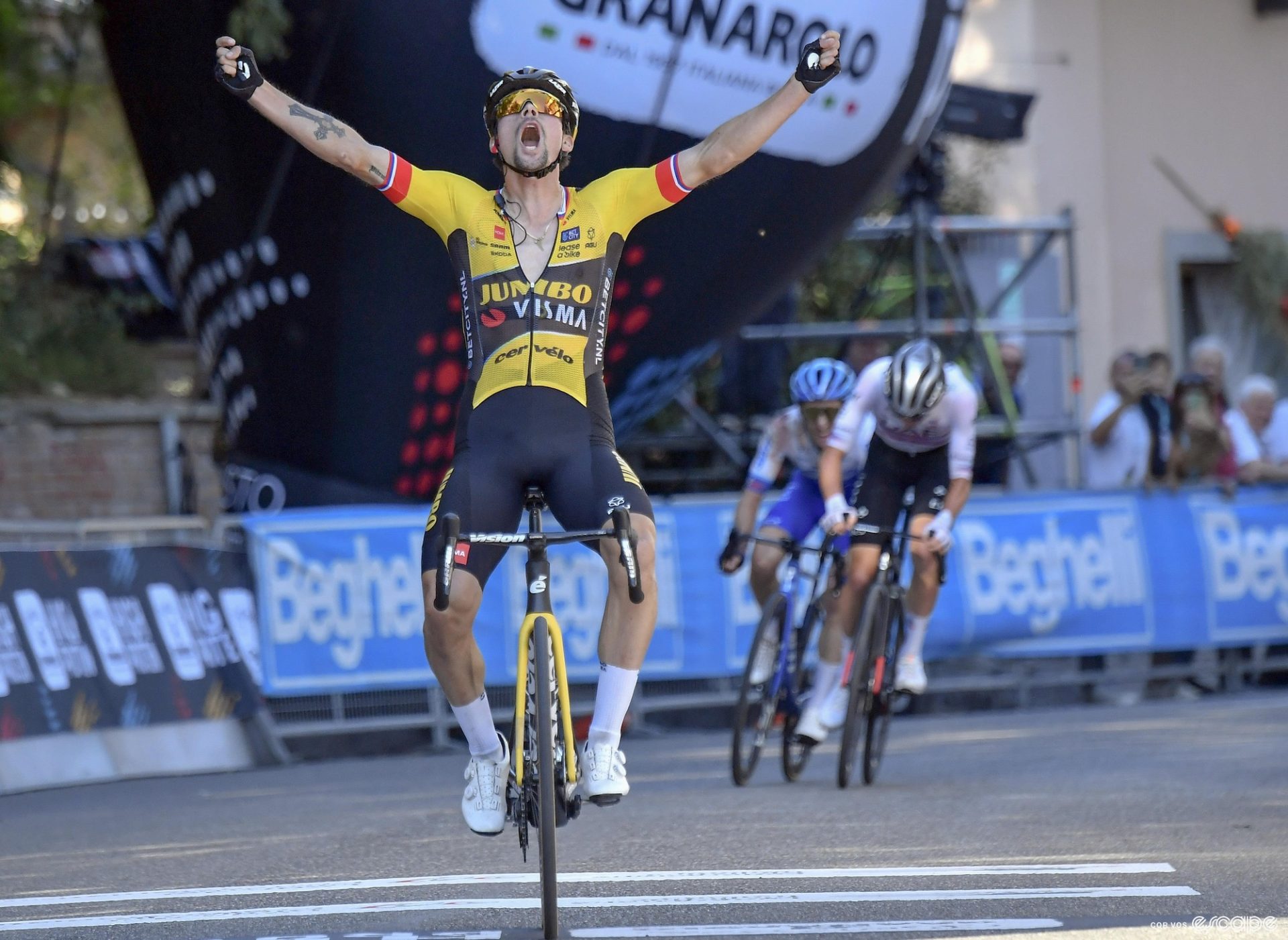 Primož Roglič wins the Giro dell'Emilia. He is crossing the line alone, arms up in a victory salute, head back in open-mouthed celebration, as Tadej Pogačar and Simon Yates sprint behind for second.