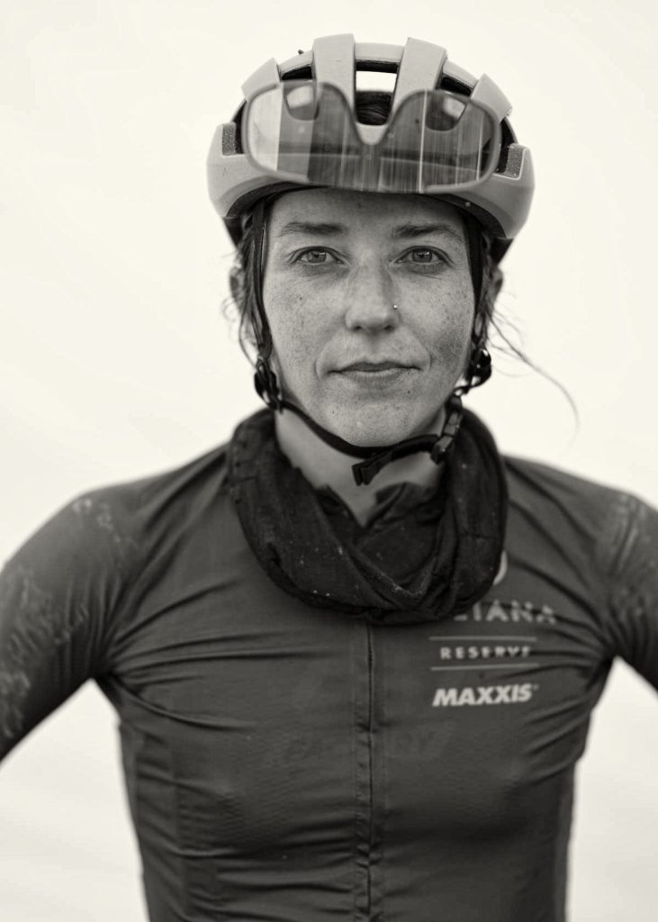 Another racer, Kaysee Armstrong, poses for her portrait, with a confident expression and hands on hips.