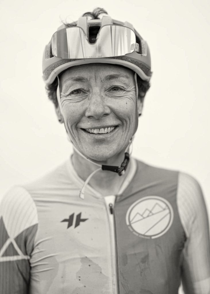 A female Breck Epic racer smiles for her portrait post-stage, with her sunglasses tucked into her helmet vents.