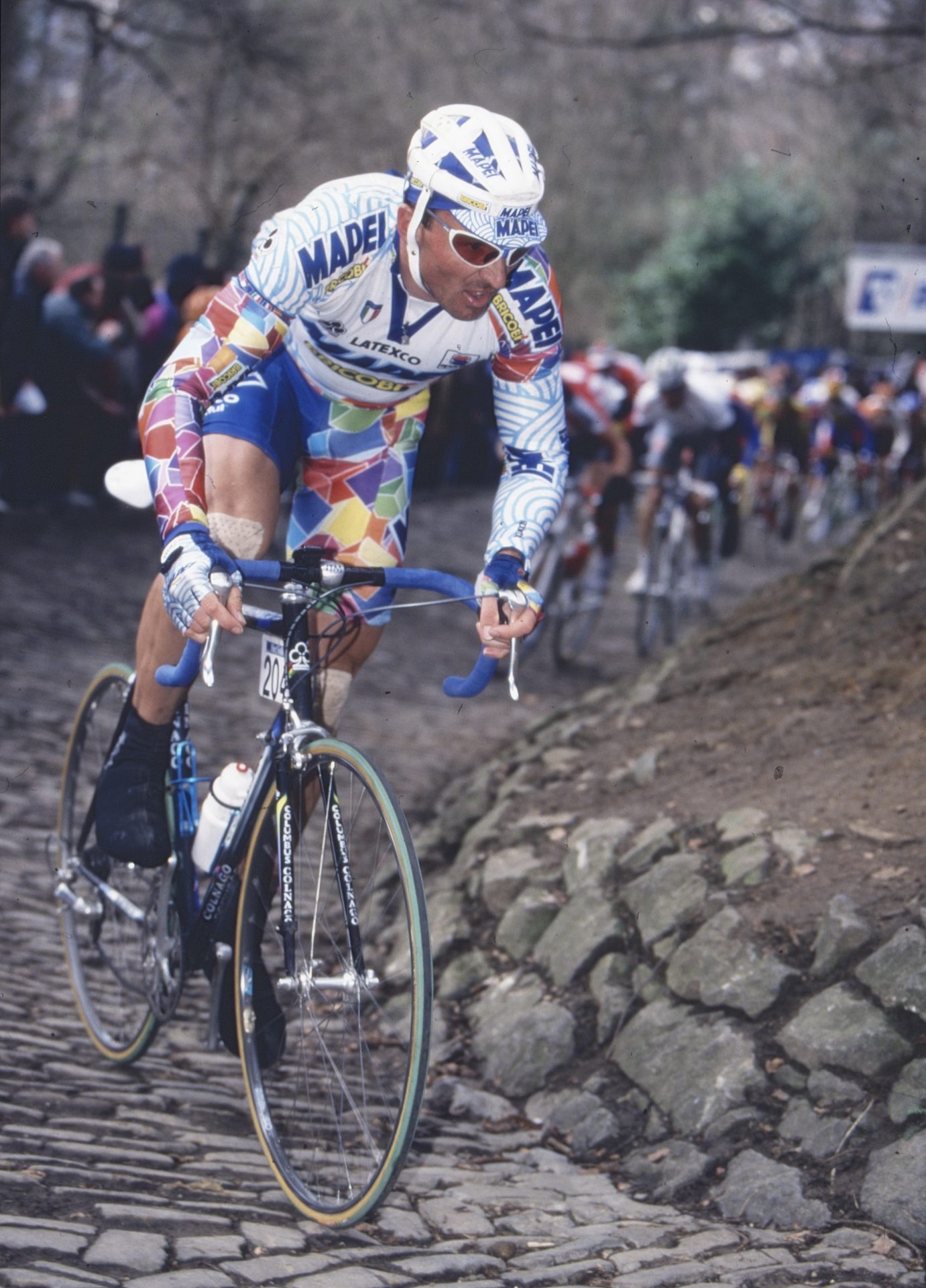 Johan Museeuw races up a berg in an edition of the Tour of Flanders. He's wearing the unmistakable multi-colored "cube" kit of Mapei as he attacks out of the saddle.
