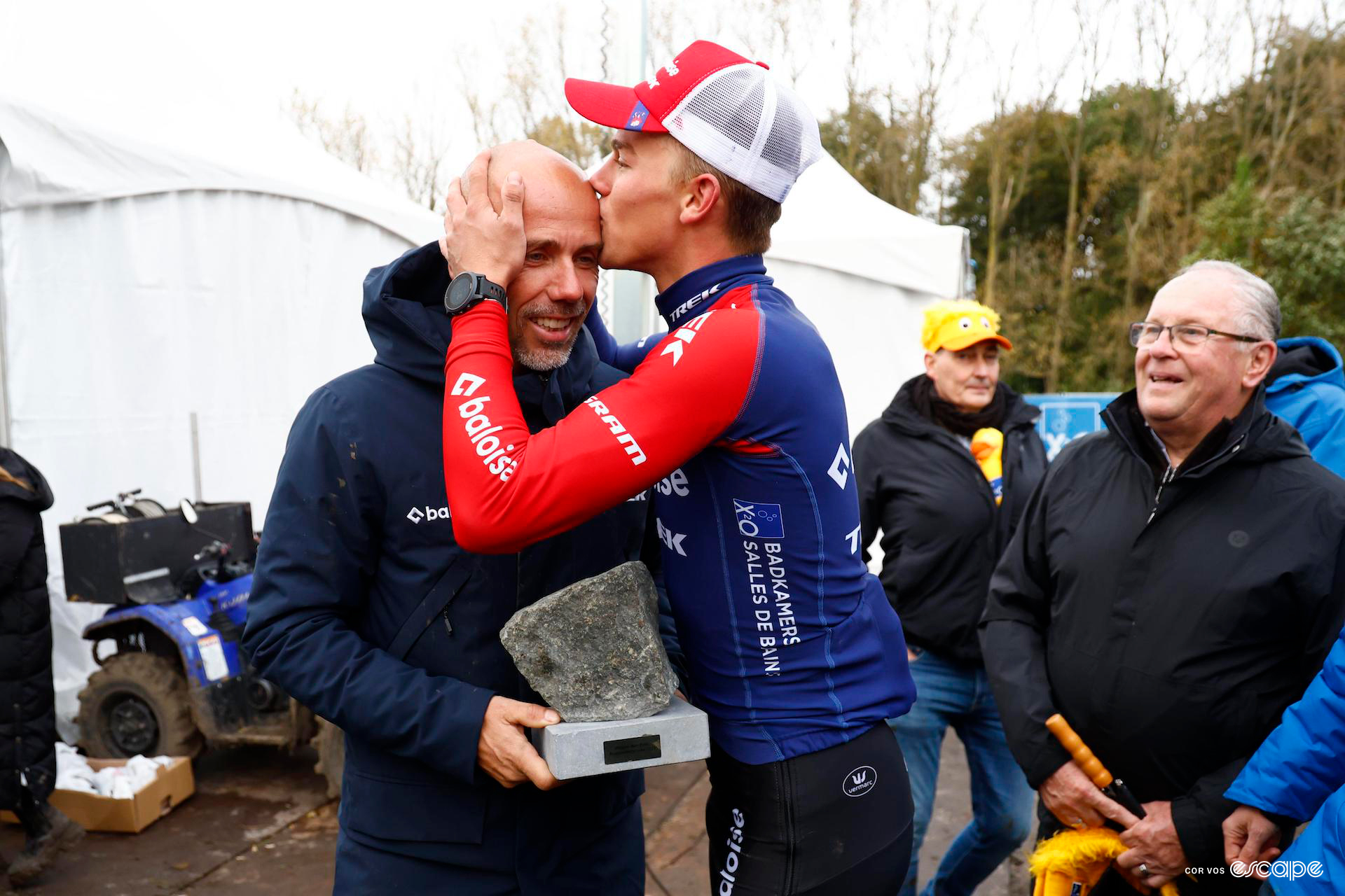 Thibau Nys kisses the top of his father's head, Sven holding the Koppenbergcross cobble trophy.
