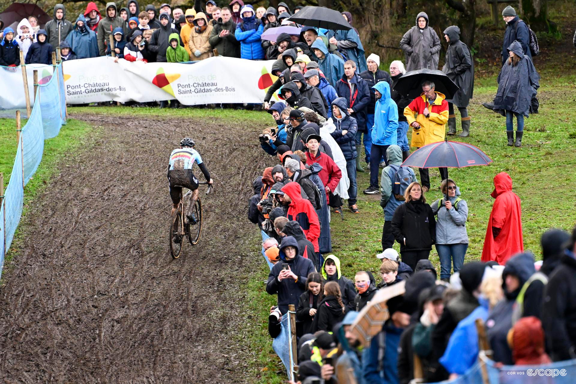 Michael Vanthourenhout of Belgium rides away through thick mud, crowds lining the fence, umbrellas raised, during the european cyclocross champs.