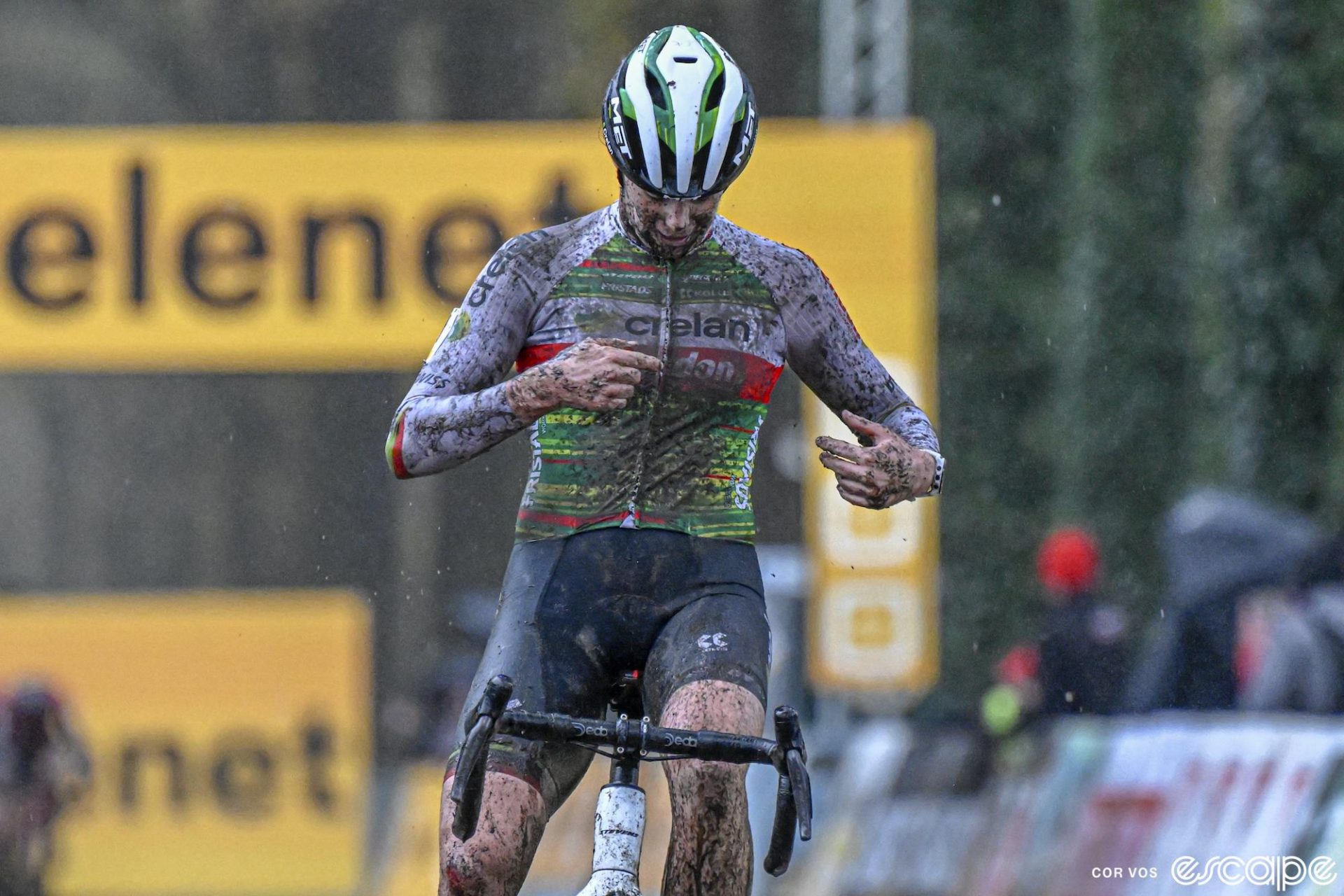 Marion Norbert Riberolle cleans mud off her jersey to point to the Crelan-Corendon logo as she crosses the line for third place.