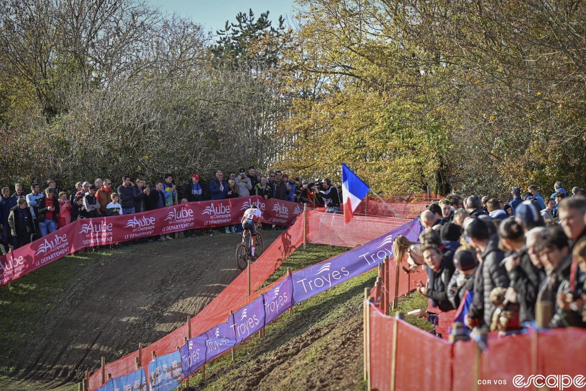 Ceylin del Carmen Alvarado rides up a small incline at Troyes. She's shown in the distance, amid large crowds in warm light, and no other racers are visible.