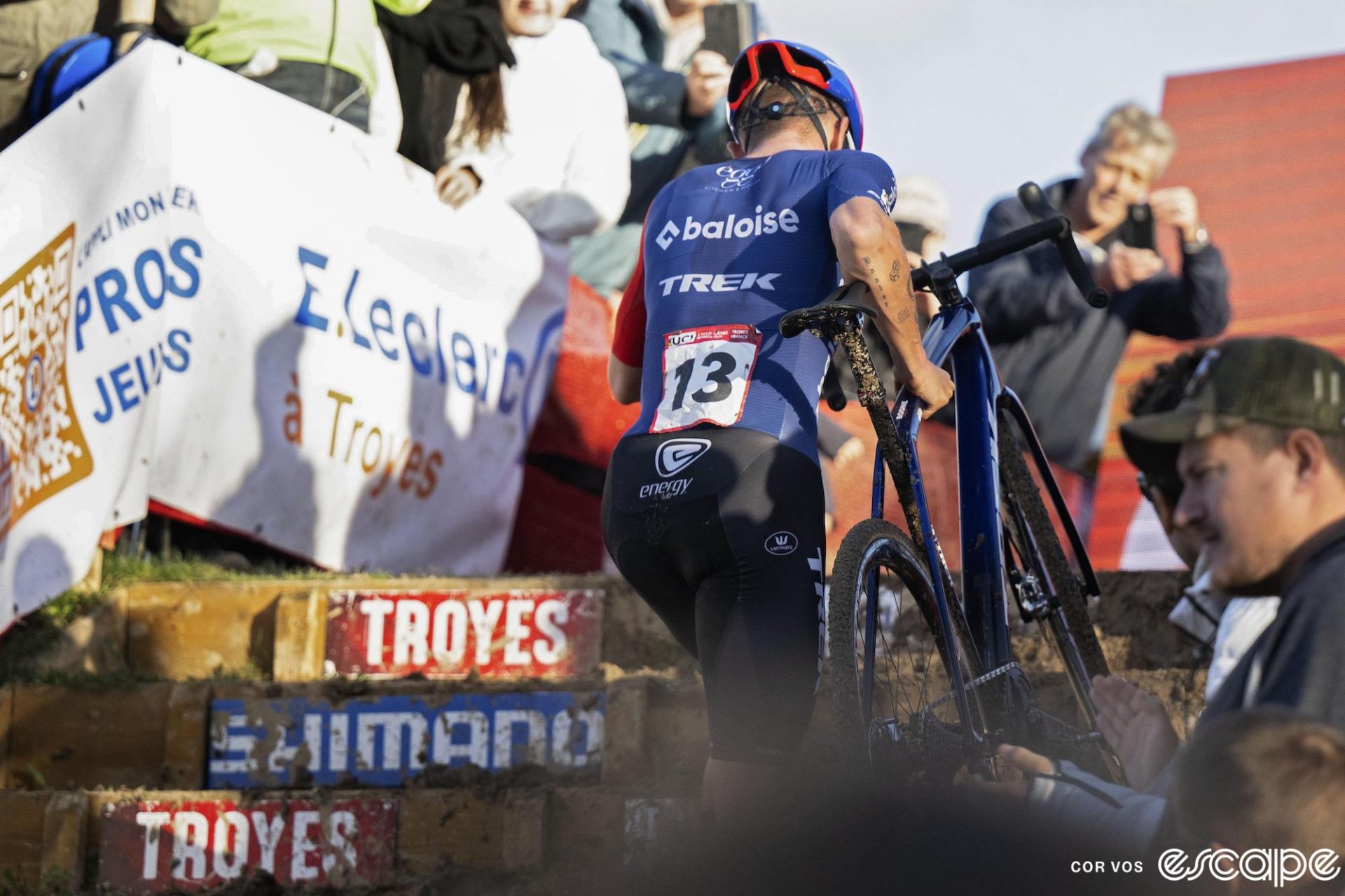 Thibau Nys suitcases his bike up the stairs at Troyes. He's shown from behind, with bib number 13.