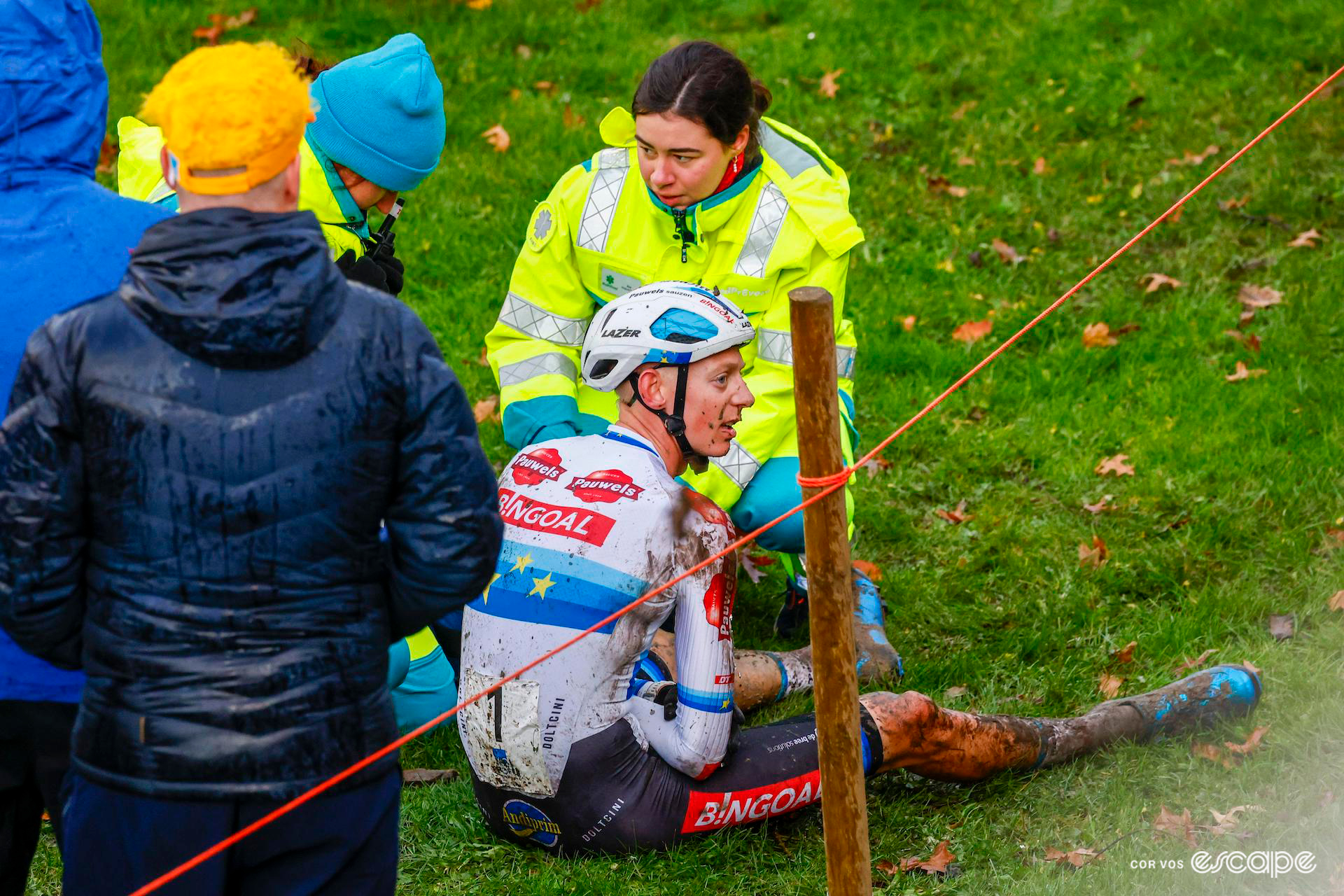 European champion Michael Vanthourenhout, splattered with wet mud, sits on the grass just off the course after crashing out of the lead of X20 Trofee Kortrijk, as two paramedics assess his dislocated shoulder.