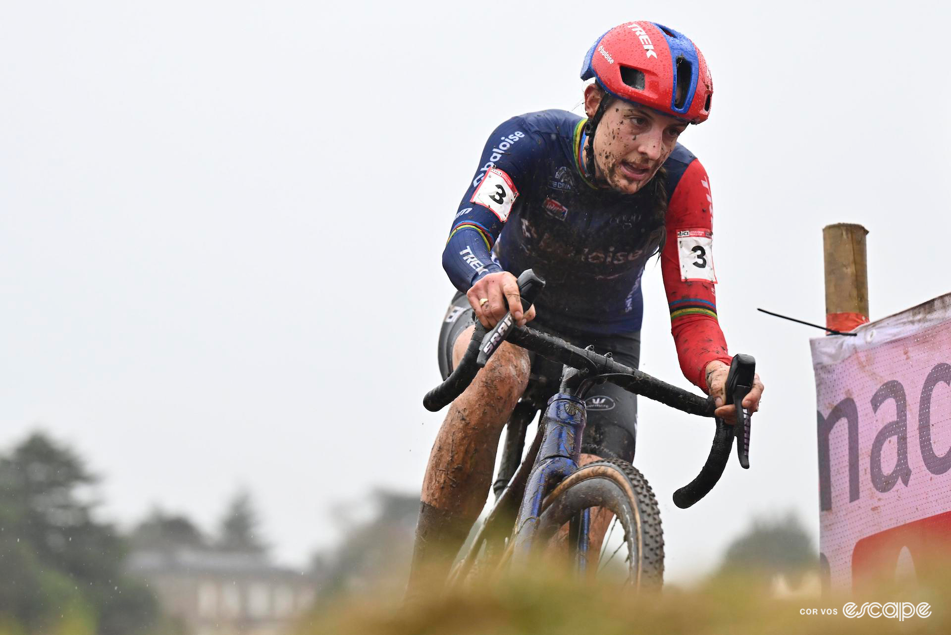Former world champion Lucinda Brand of Baloise Trek Lions takes a corner during CX World Cup Dublin, her legs and kit splashed with mud, an overcast sky overhead.