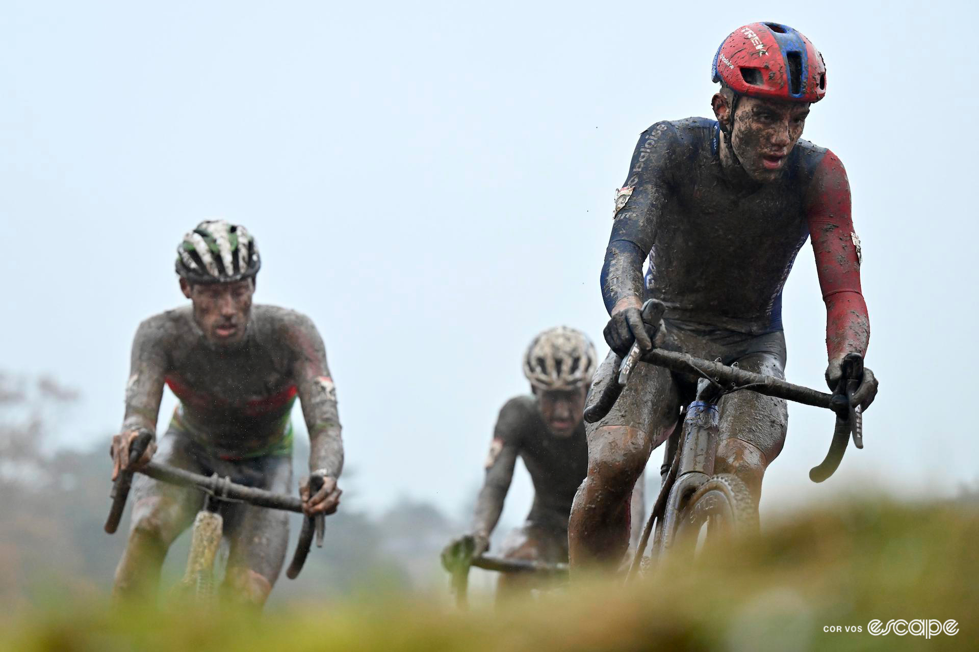 Thibau Nys leads Joran Wyseure and Jens Adams, all of them covered head to toe in mud and looking very weary, late in CX World Cup Dublin, a grey overcast sky overhead.