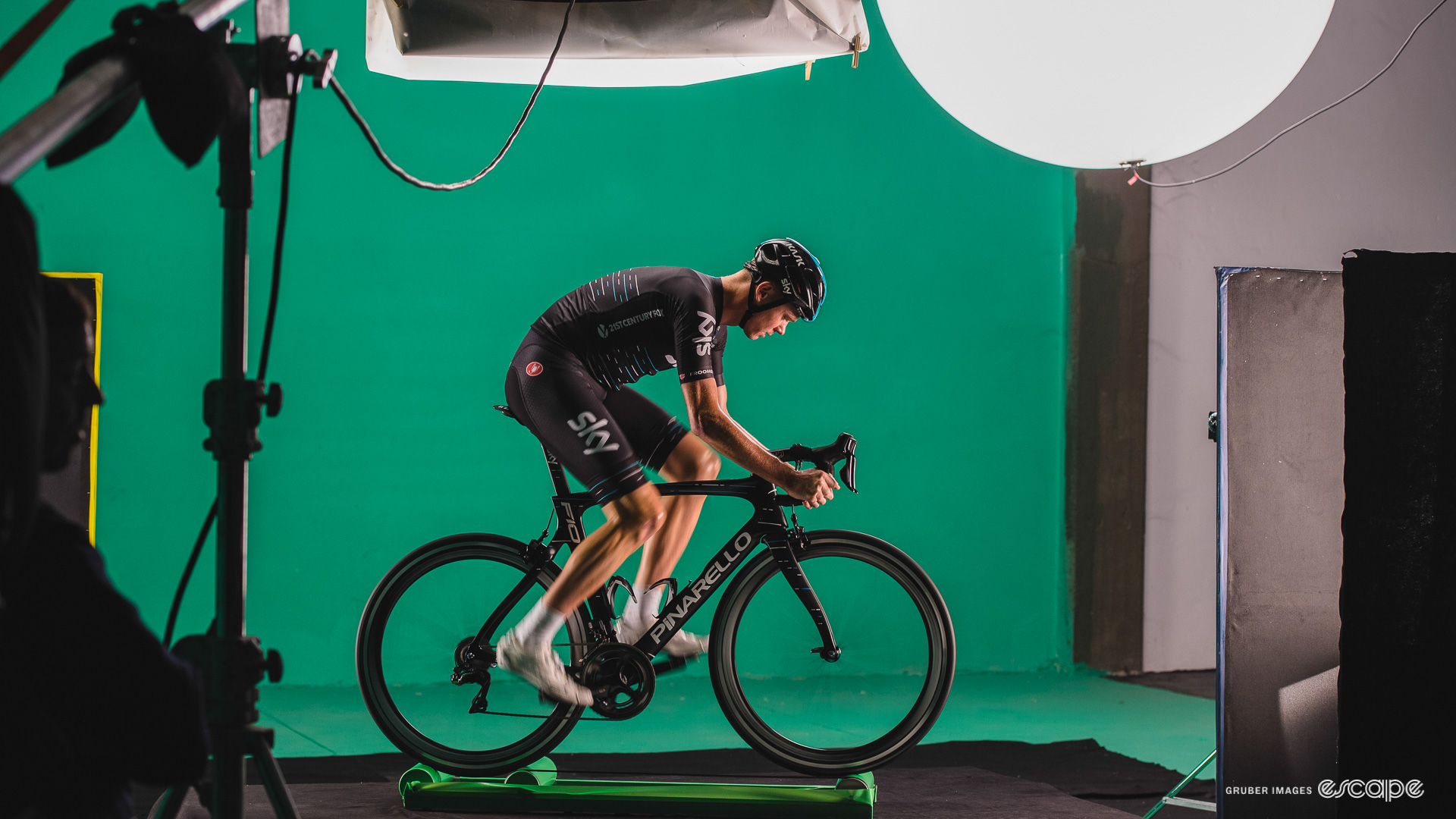 The photo shows Chris Froome riding a Pinarello F8 on rollers in front of a green screen