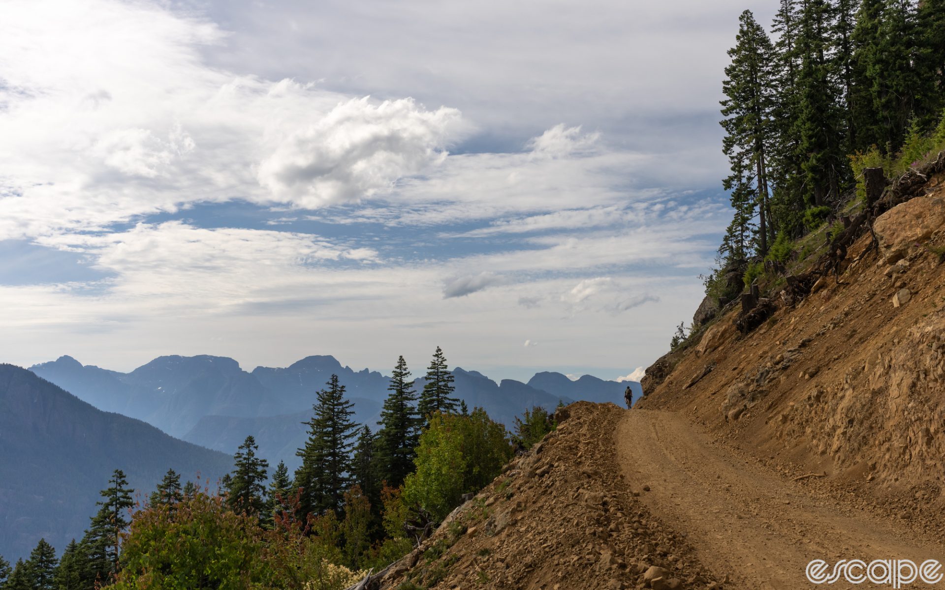 A bikepacker rides an unimproved dirt road high in the mountains. The rider is in the distance, all alone against a silhouette of purple peaks in the background.