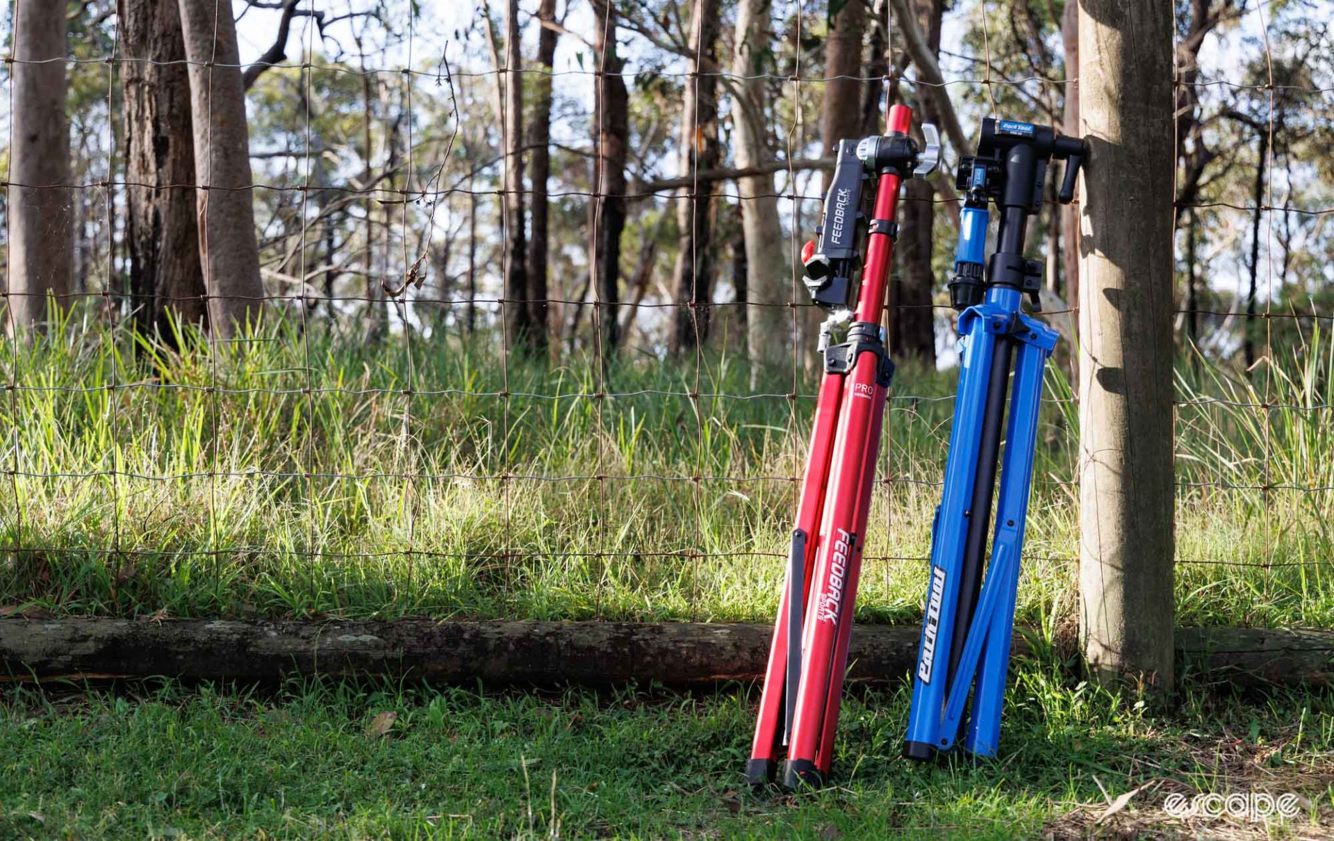 Park Tool PRS-26 and Feedback Sports Pro Mechanic repair stands folded up, leaning against a fence. 