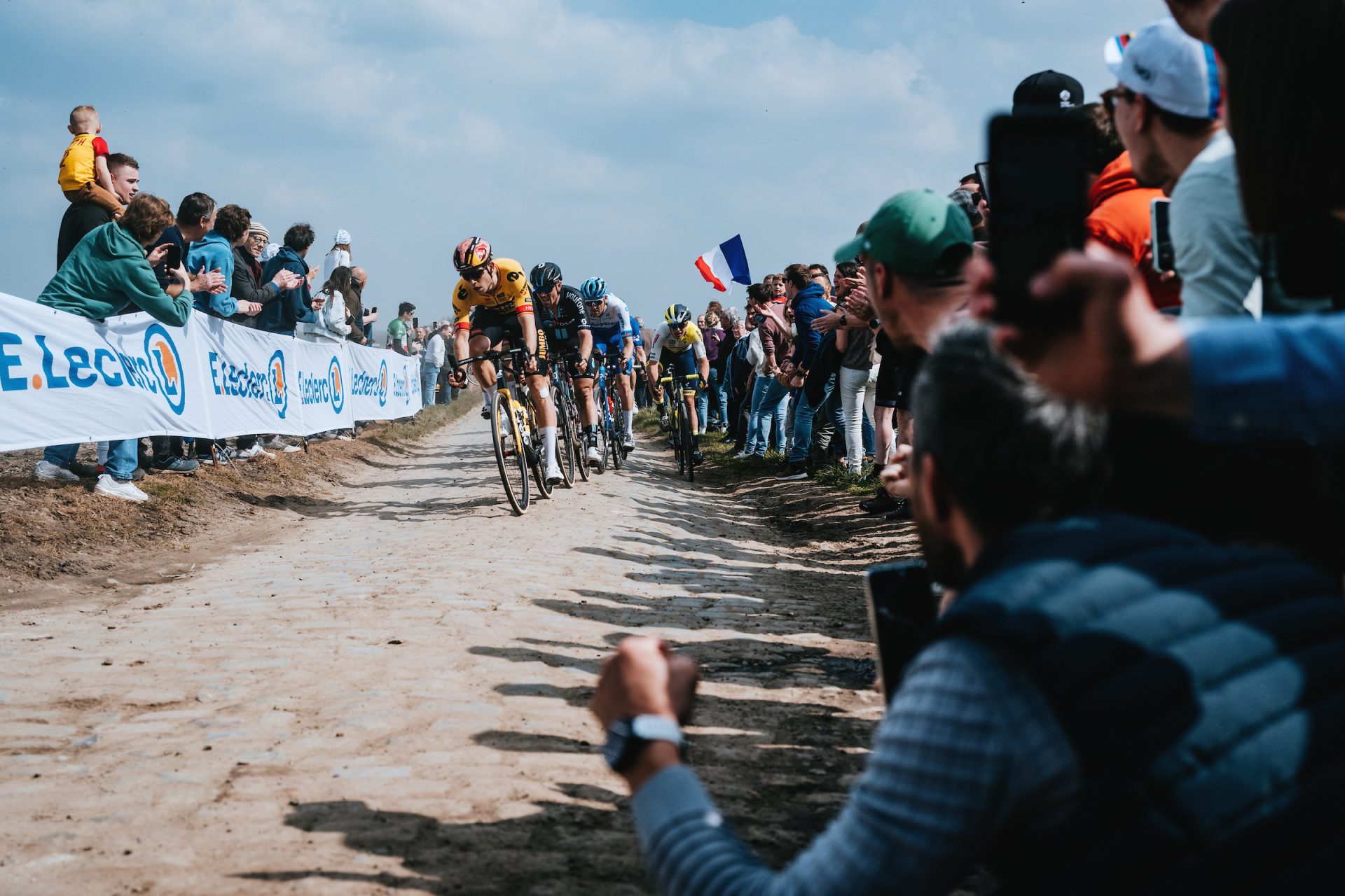 Wout van Aert leads the selection across dry and dusty cobbles. Throngs of fans crowd the edge of the lane.
