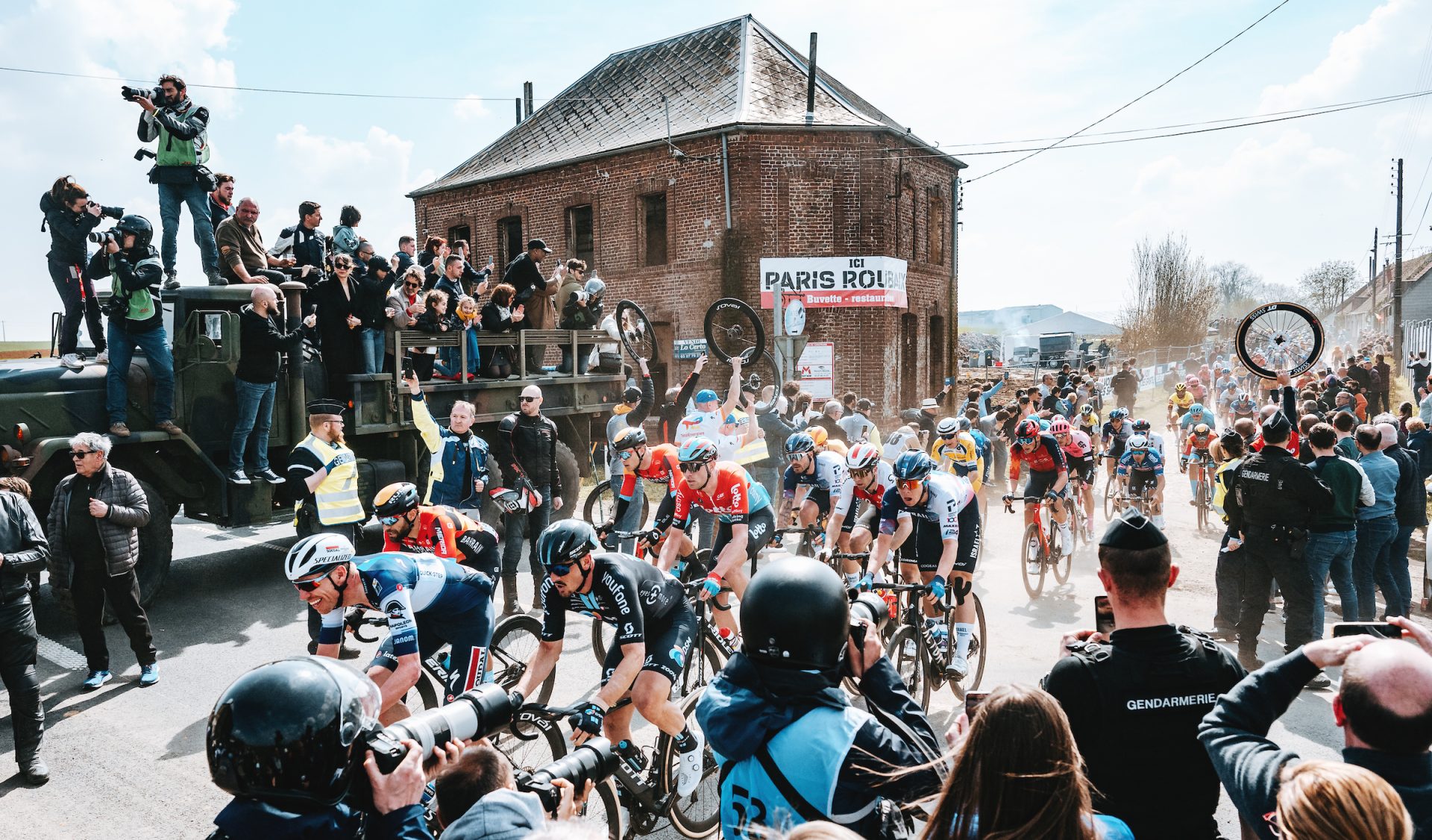 The chaos at the exit of a secteur of pavé, with crowds of photographers, fans and soigneurs with spare wheels watch the peloton scream past.