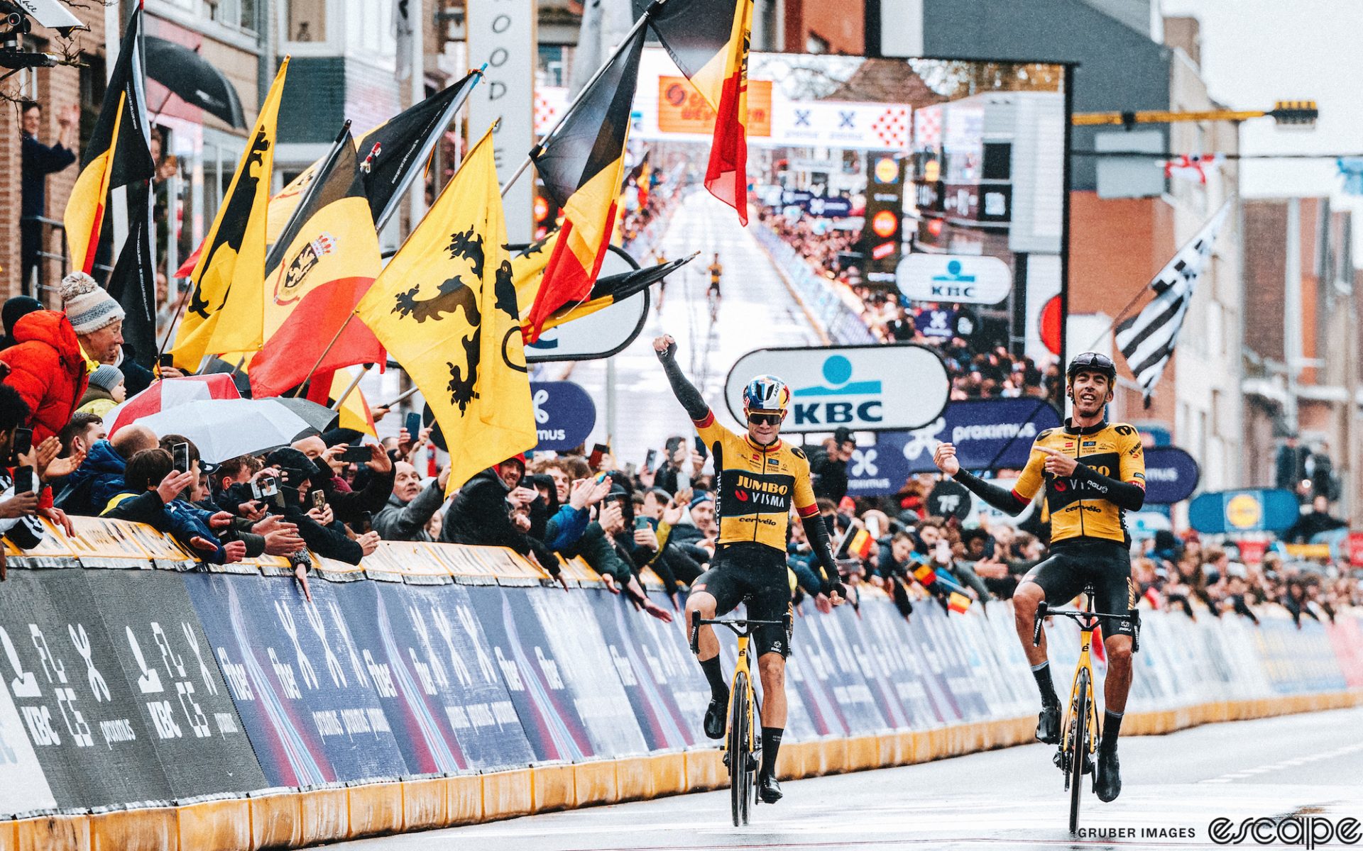 Christophe Laporte and Wout van Aert go 1-2 at the 2023 Gent-Wevelgem. The pair is crossing the finish line well in front of the chase. Wout has a fist in the air while Laporte is pointing to his teammate.
