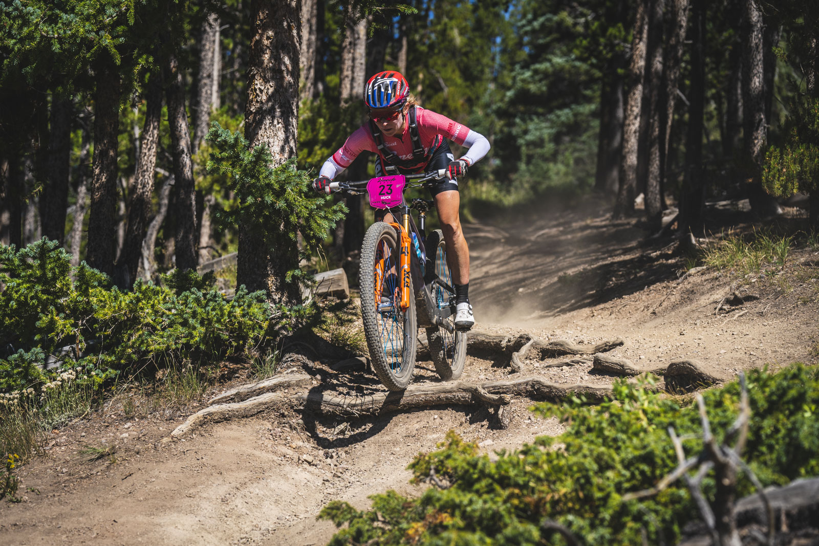The aptly named Erin Huck shreds a descent at the 2023 Breck Epic. She's boosting off a root and in attack position, arms bent, as the front wheel goes airborne.