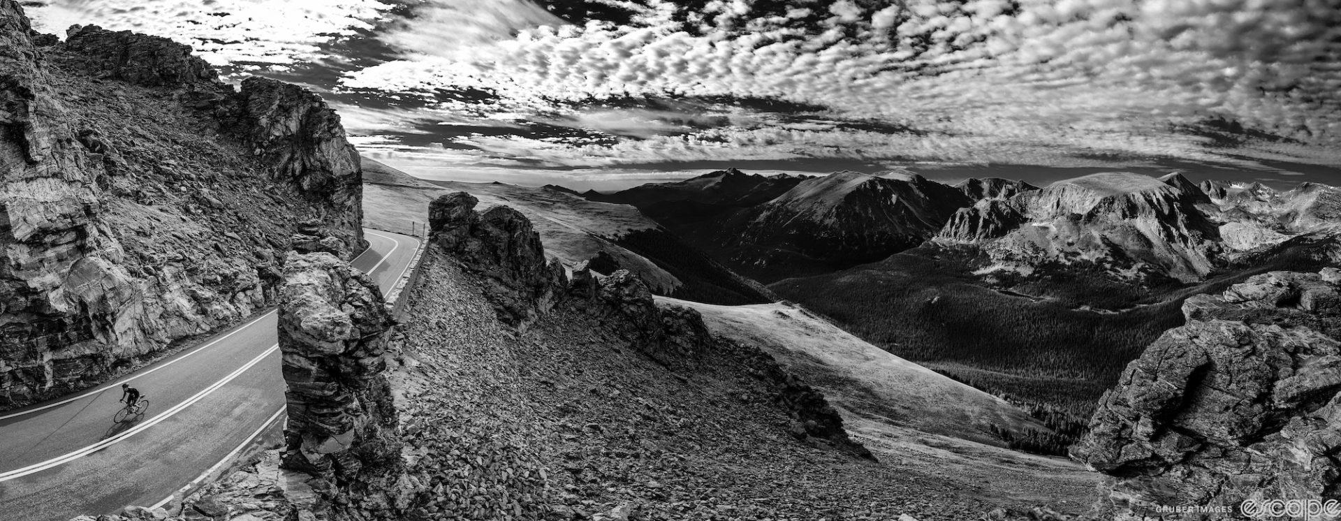 A lone rider climbs on a moon-like rockscape high in the Colorado Rockies in this black and white shot, with white clouds popping against a dark sky.