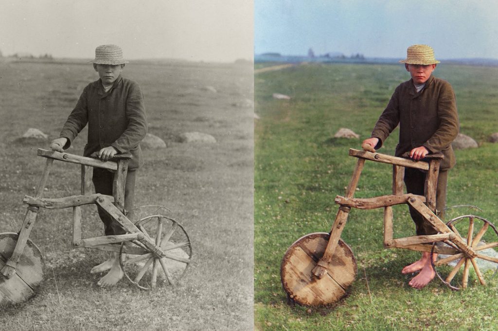 A boy with a wooden bike stands in a field in rural Estonia.