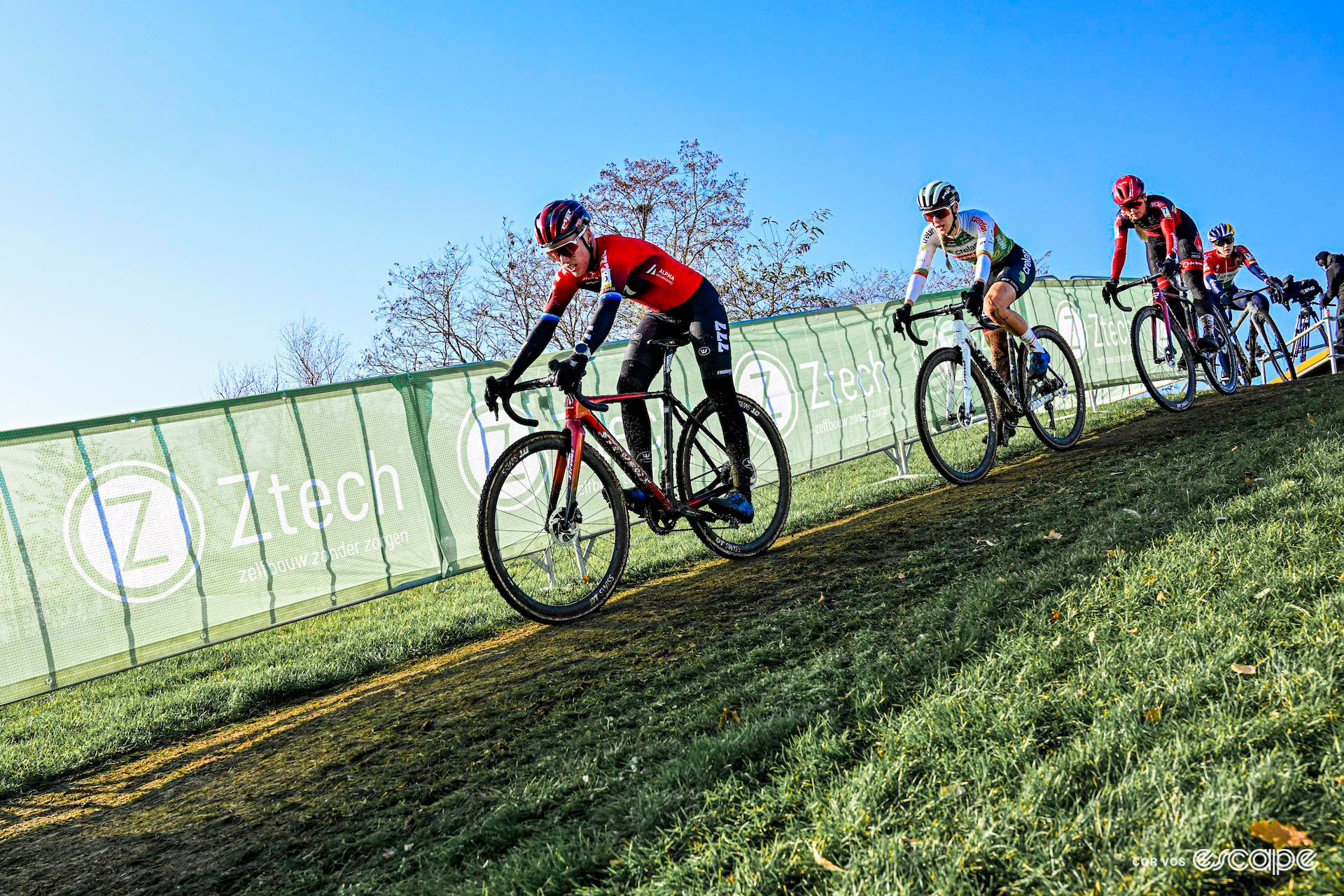 Annemerie Worst of Cyclocross Reds leads a group on a grassy descent against a clear blue sky during Cyclocross Superprestige Boom.