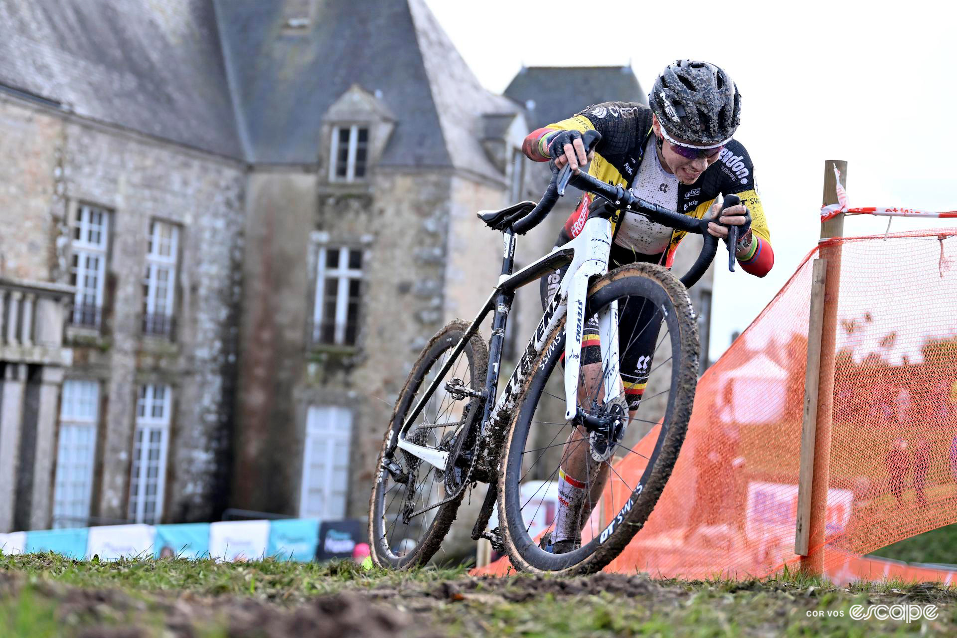 Sanne Cant's Belgian national champion's jersey is unzipped as she pushes her bike up a ramp during Cyclocross World Cup Flamanville, the castle in the background.