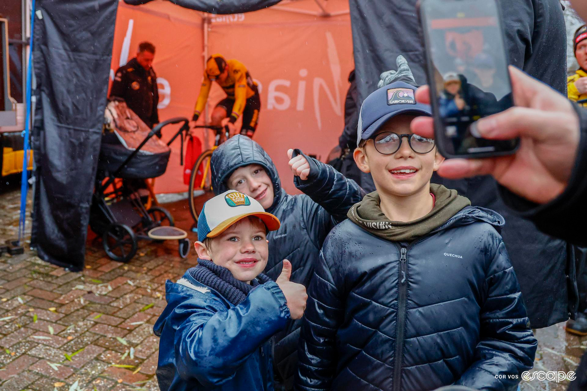Wout van Aert in the background as young fans pose for a photograph at a very wet and muddy Exact Cross Essen.