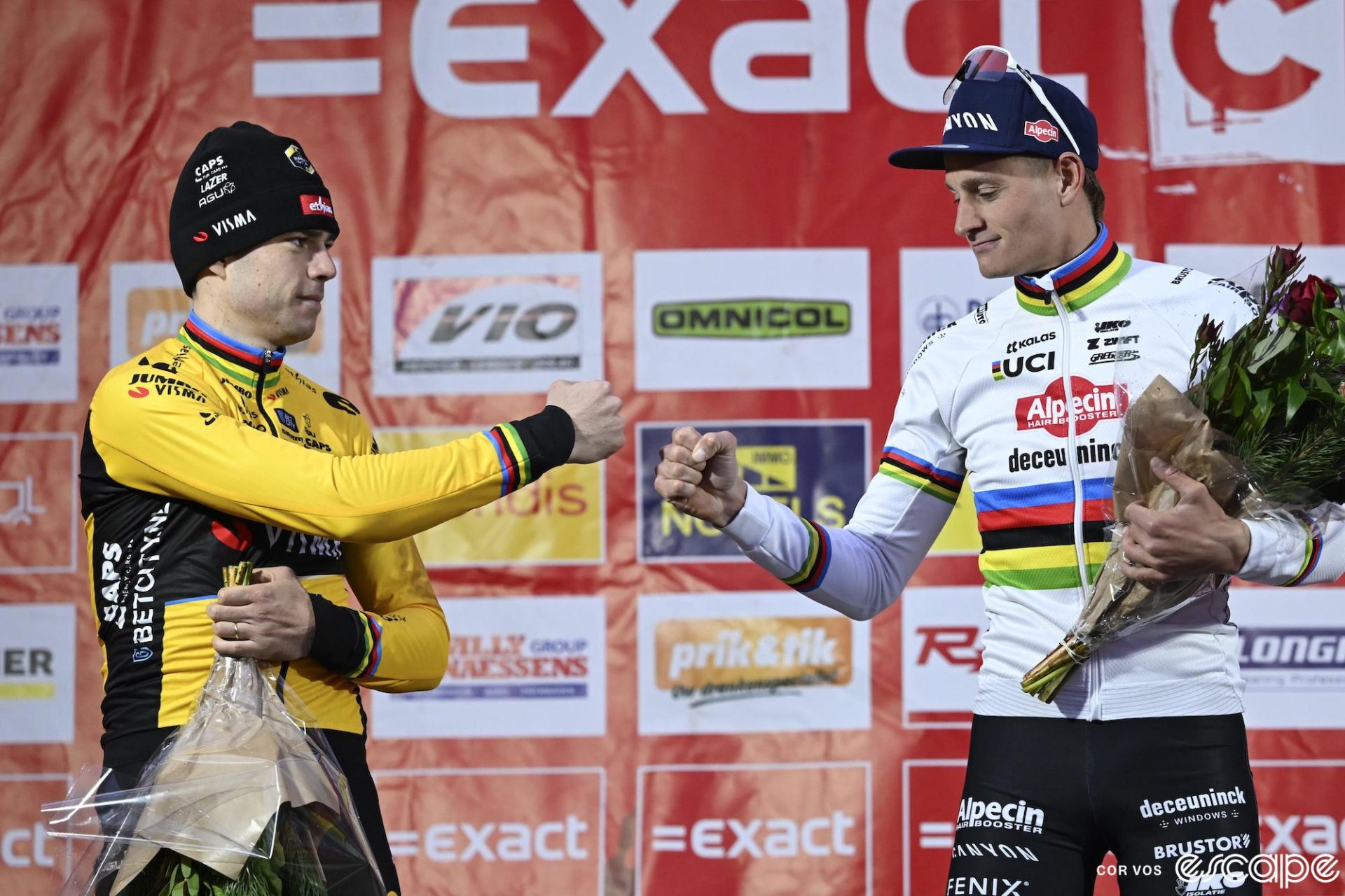 Van Aert and Van der Poel share a fist bump on the podium. Van Aert has an unreadable expresion while Van der Poel is slightly smiling.