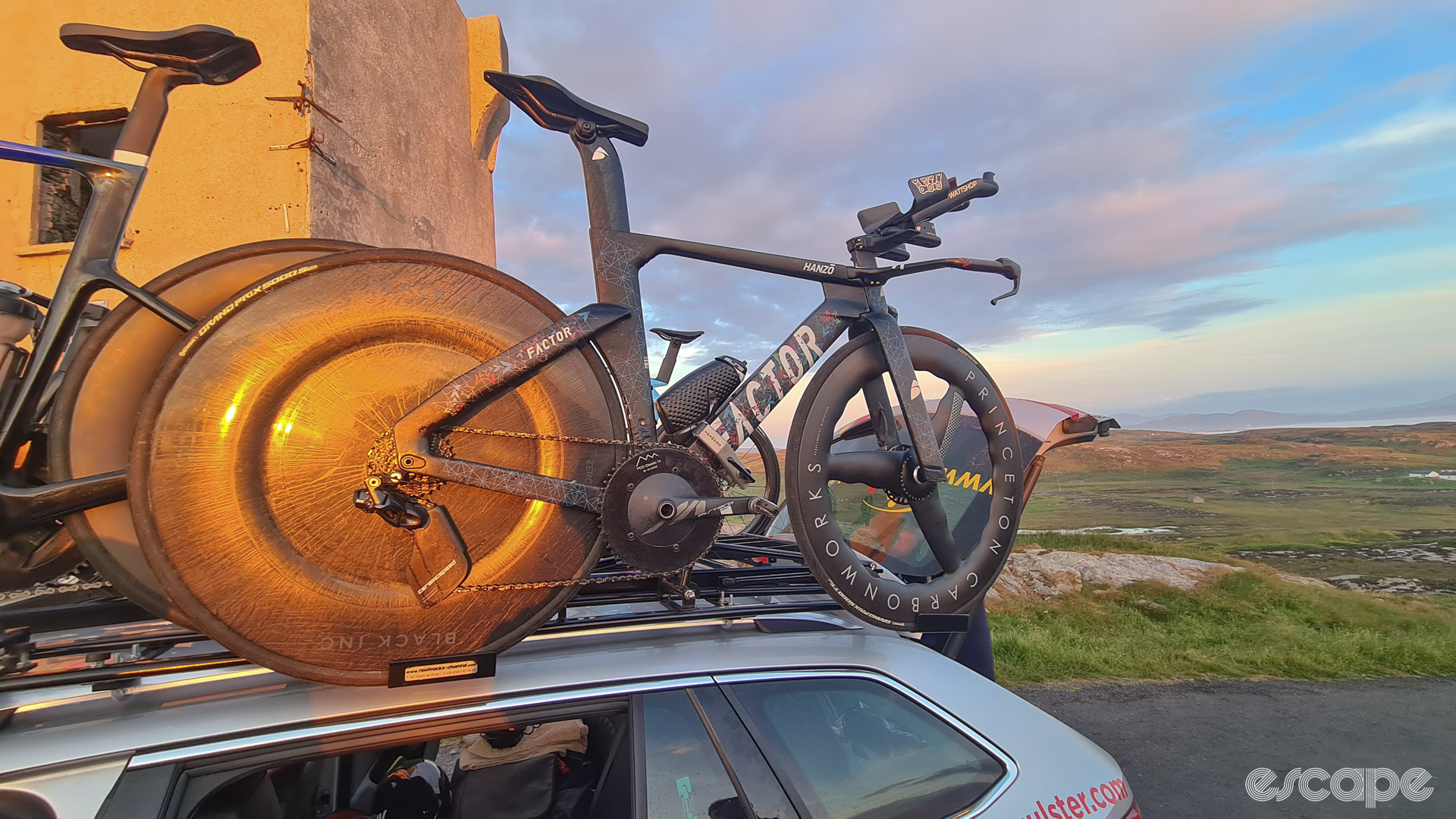 The photo shows a time trial bike on the roof of a team car