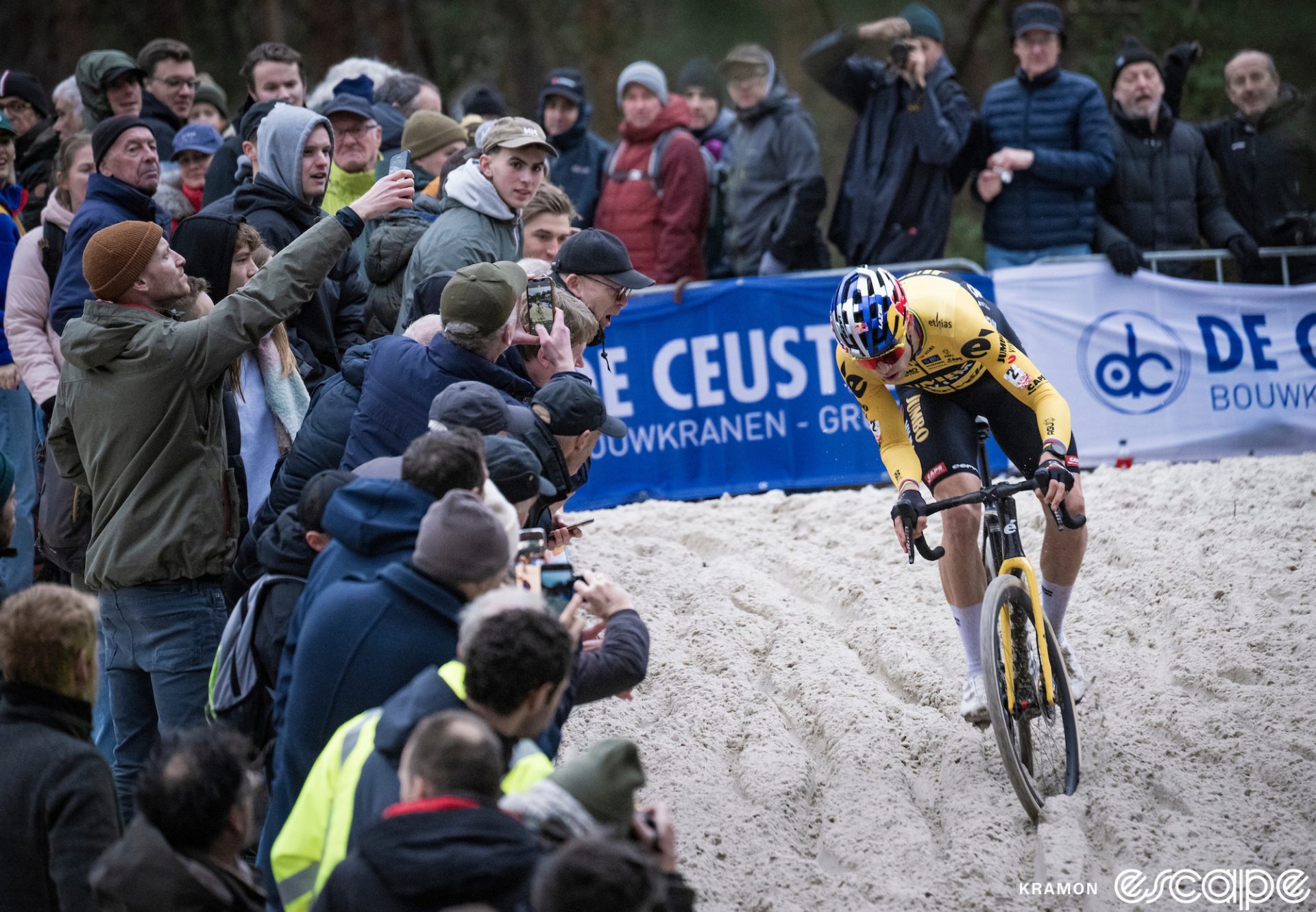 Van Aert fights to keep his bike upright and moving forward in the sand. He's leaning to his right to countersteer the bike as the front wheel slides.
