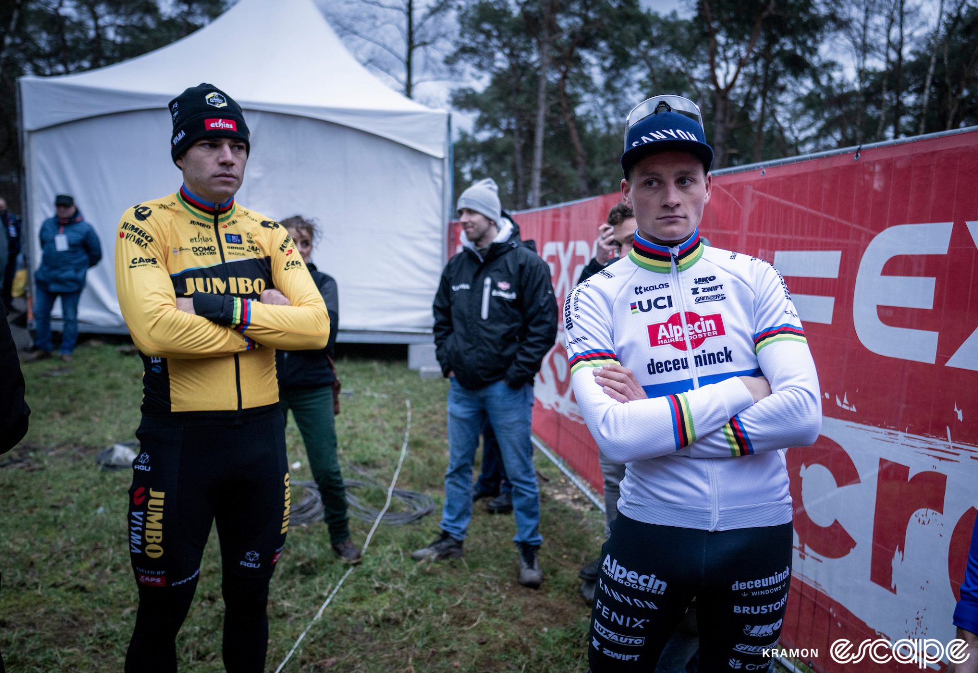Wout van Aert casts a sidelong glance at Mathieu van der Poel post-race. They're both standing with arms crossed waiting for the podium.
