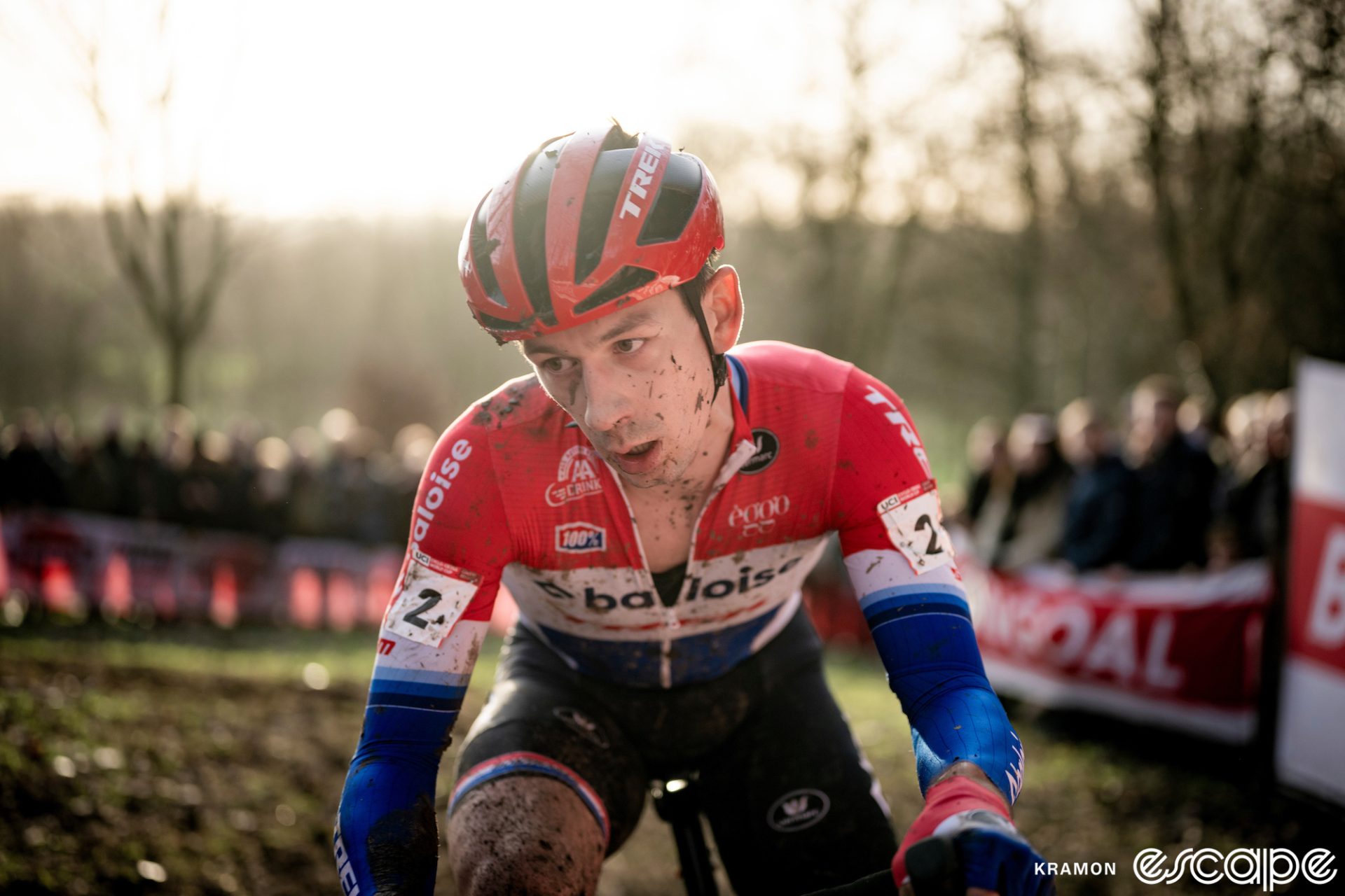 Lars van der Haar climbs a muddy section. He's shown in close-up, with warm soft light behind him.