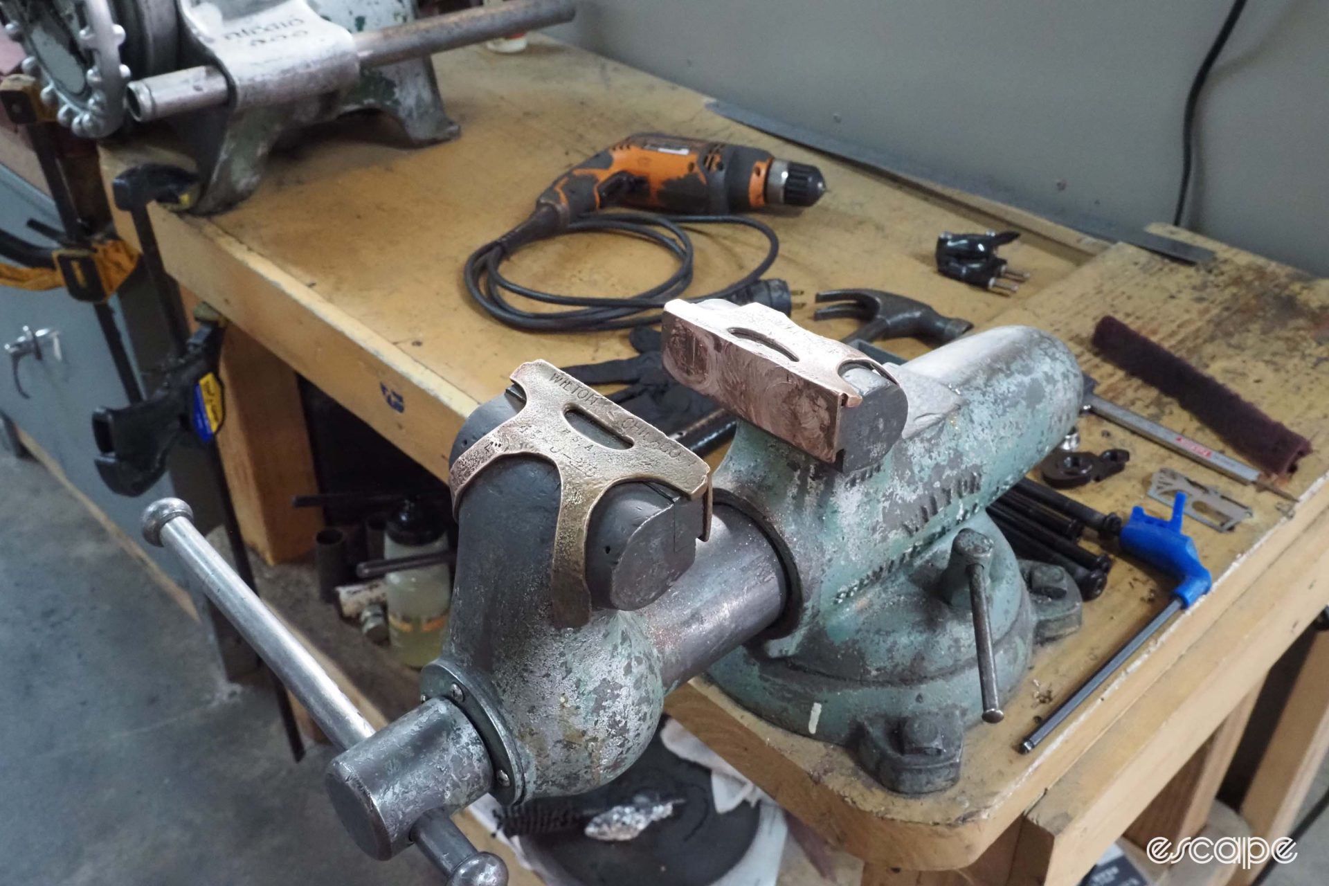 A weathered bench vise has its clamps covered in copper jaws.